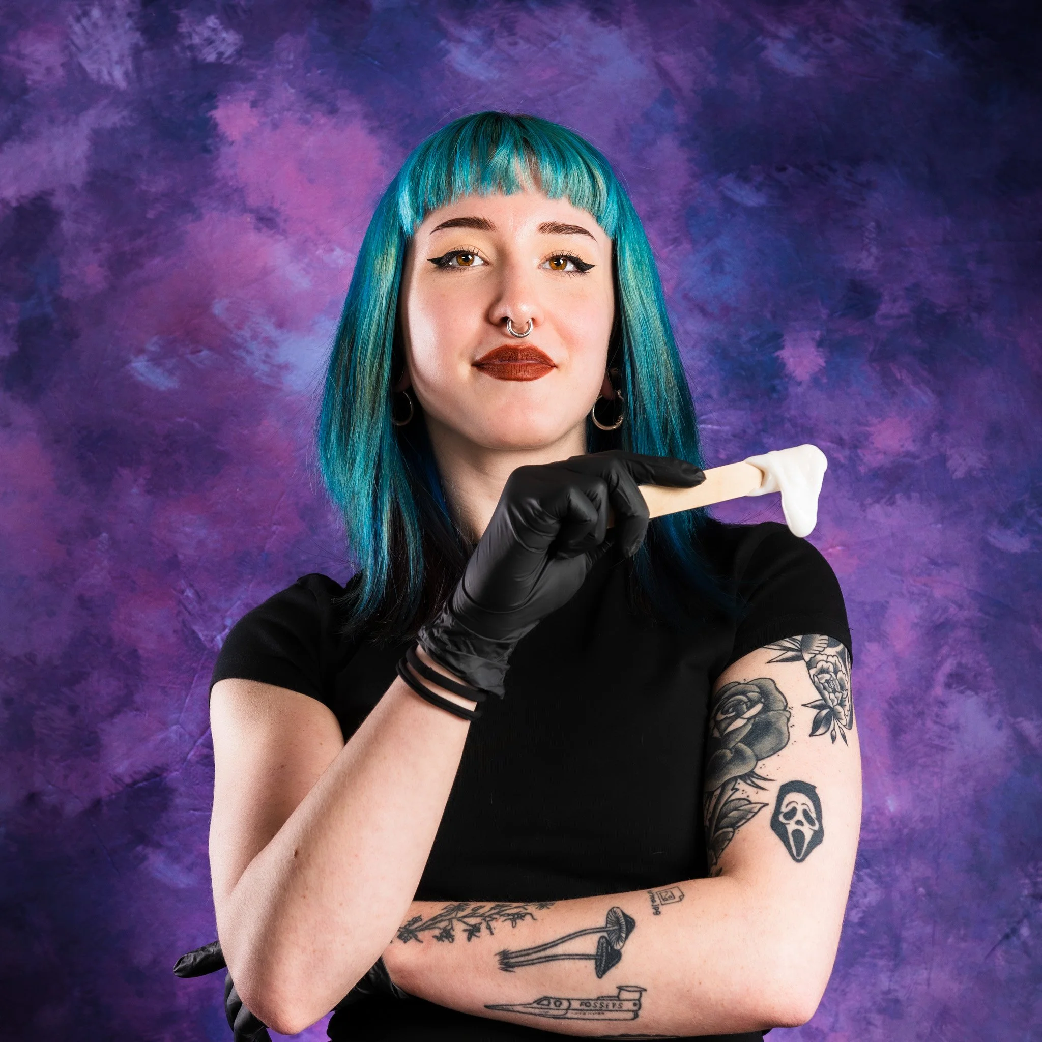 Headshot client for beauty studio holding waxing tools against a purple textured background.