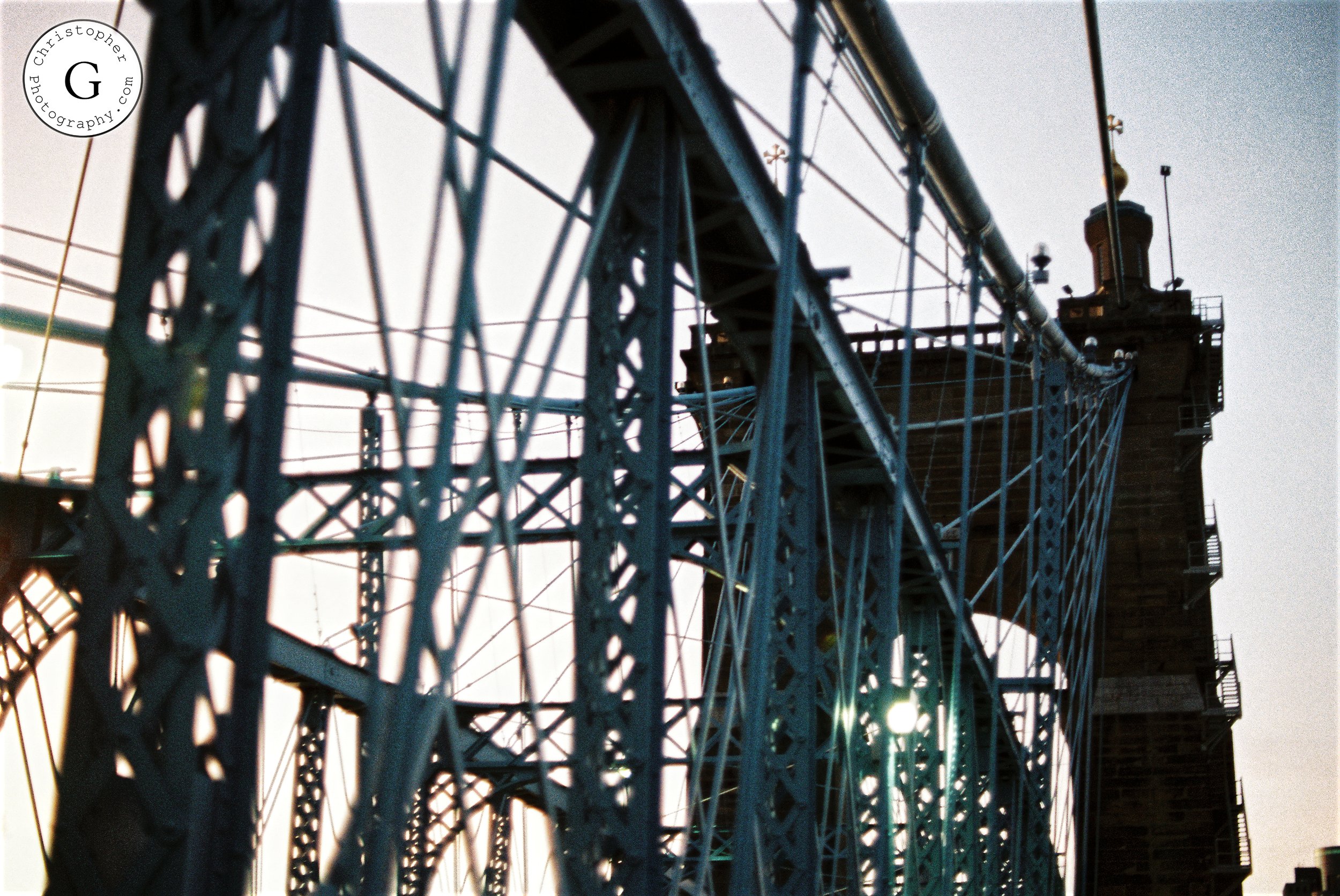 Close-up of a steel suspension bridge with a tower in the background, taken during sunset or sunrise shot on 35mm film.