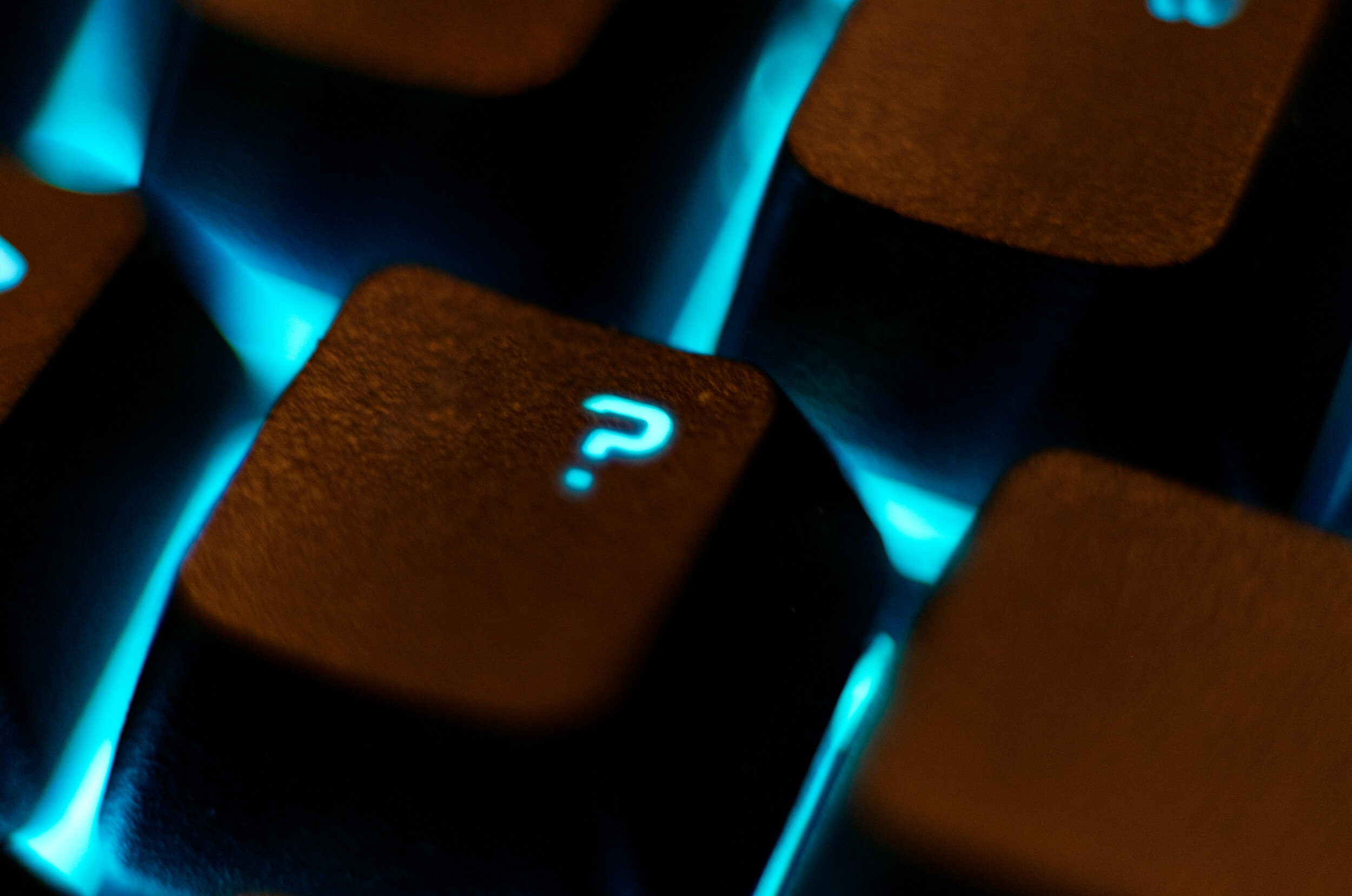 Close-up of a computer keyboard key with a question mark, illuminated with blue backlight.