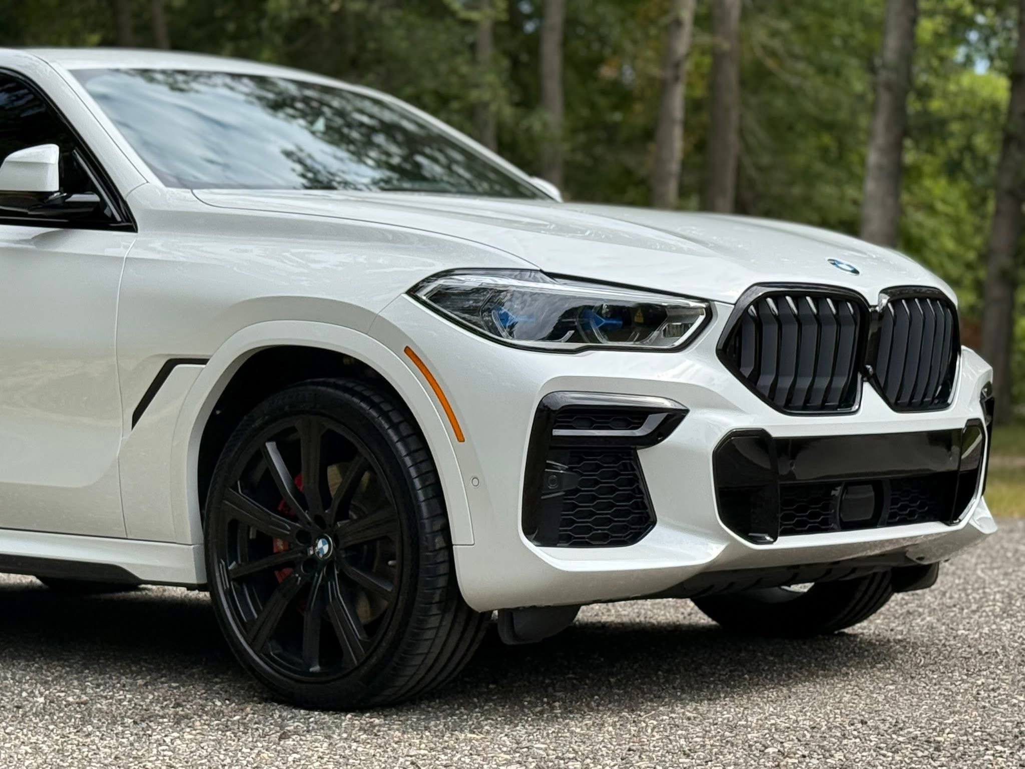 A white BMW SUV parked outdoors with a background of trees and a cloudy sky reflected on the windshield.