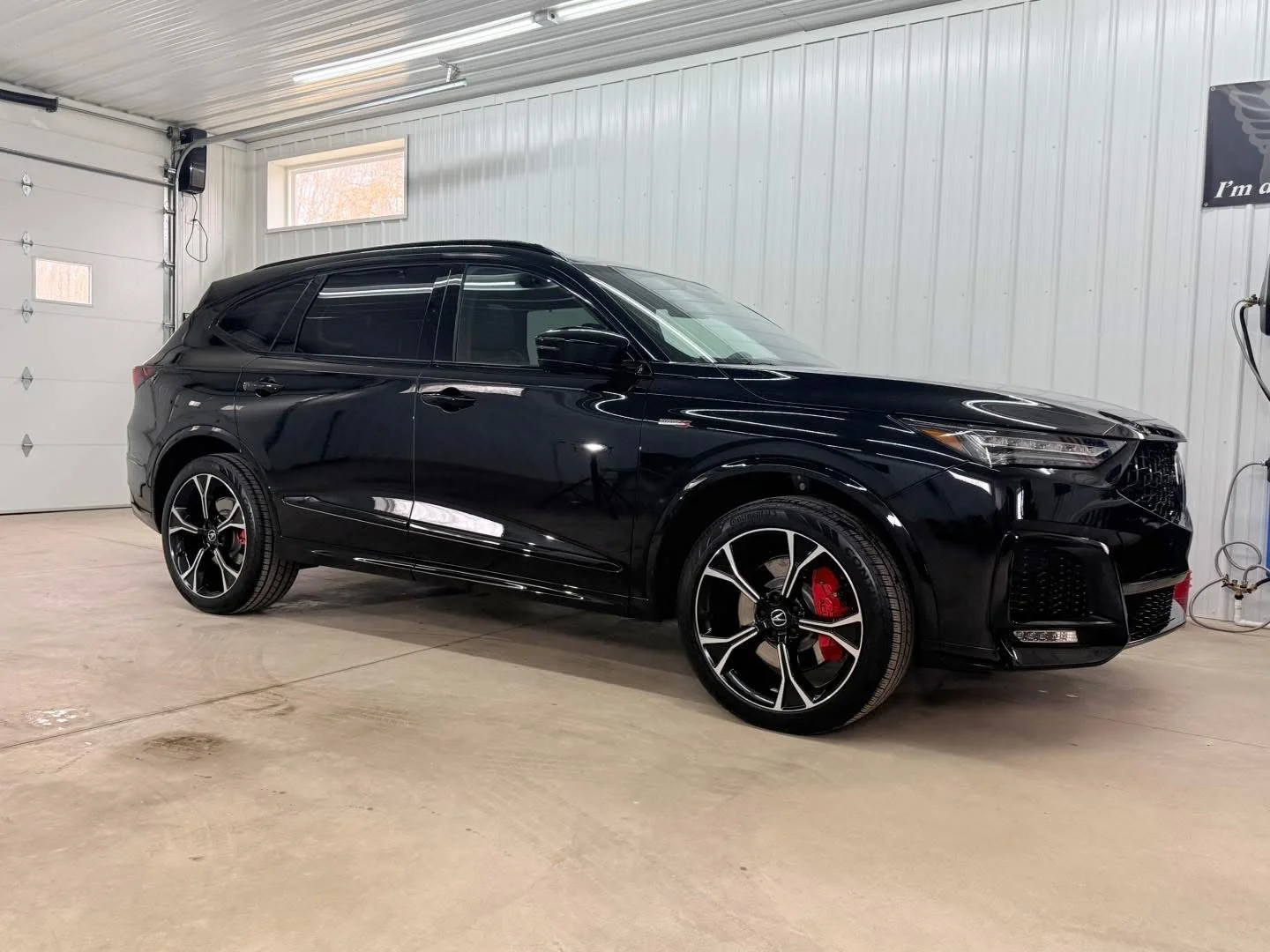 Black SUV parked inside a garage with white walls, a small window, and a closed garage door.