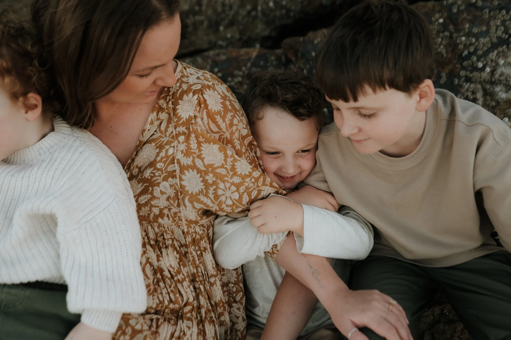 A woman and three children sitting close together outdoors, embracing and smiling.