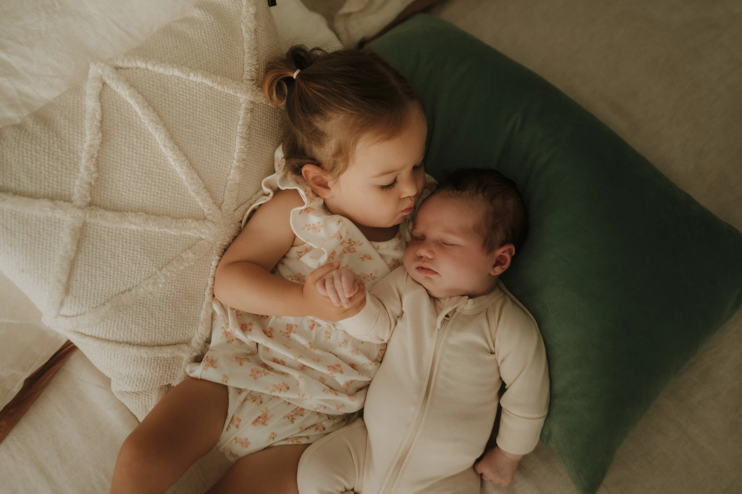 Two young children, a girl and a boy, lying on a bed, holding hands, with their eyes closed, appearing to be sleeping or resting.