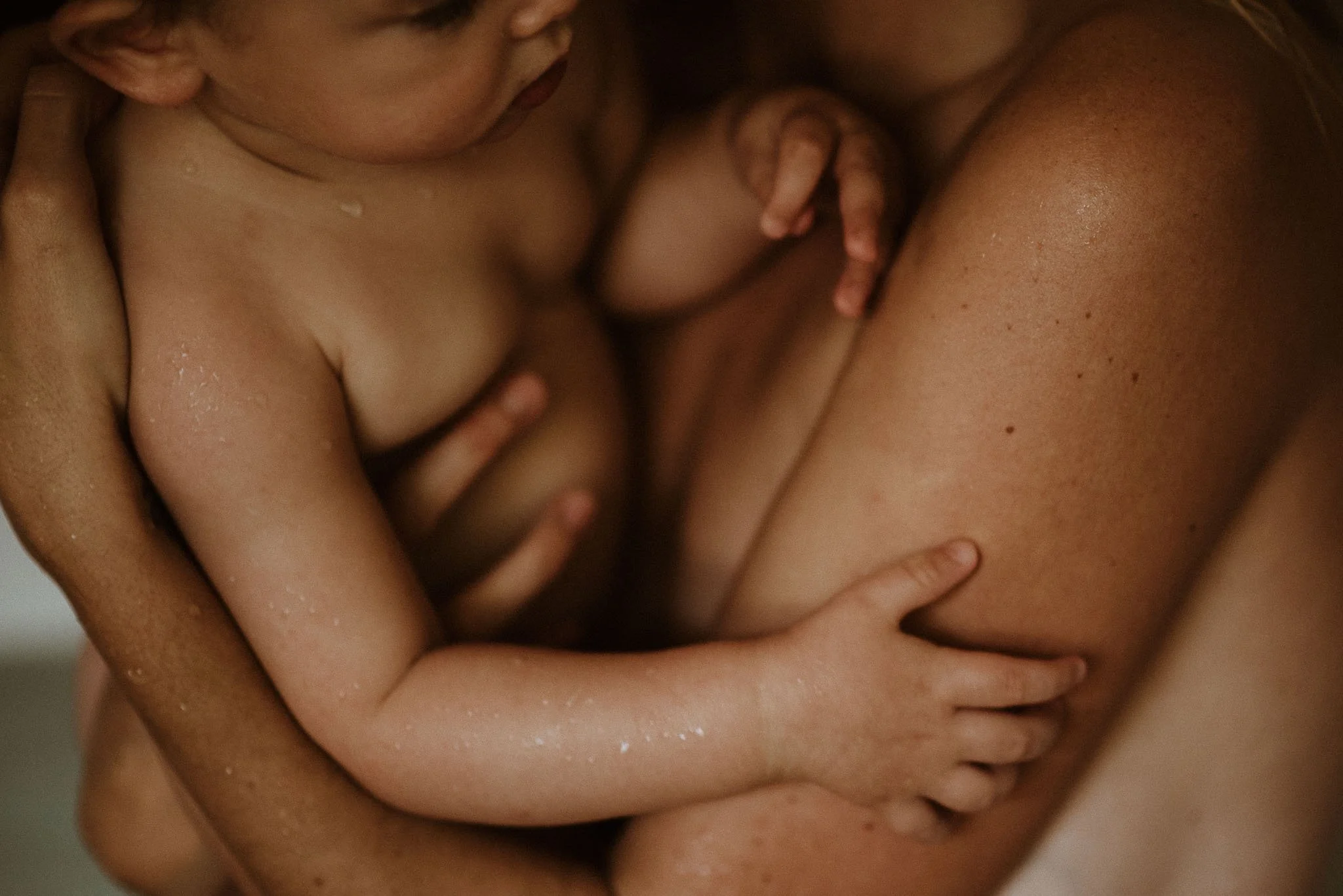 Close-up of baby being held, showing bare skin and intimate bonding.