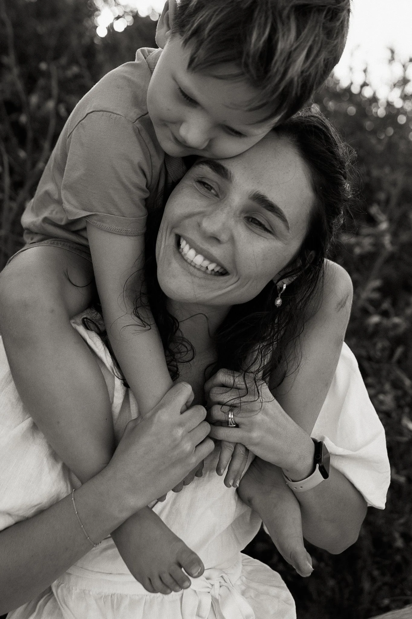 A woman smiling and holding a child on her shoulders outdoors.