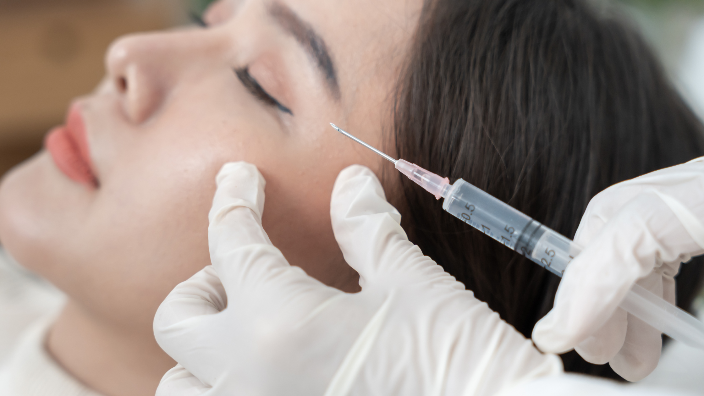 A person lying down receiving an injection in the face from a medical professional wearing gloves.