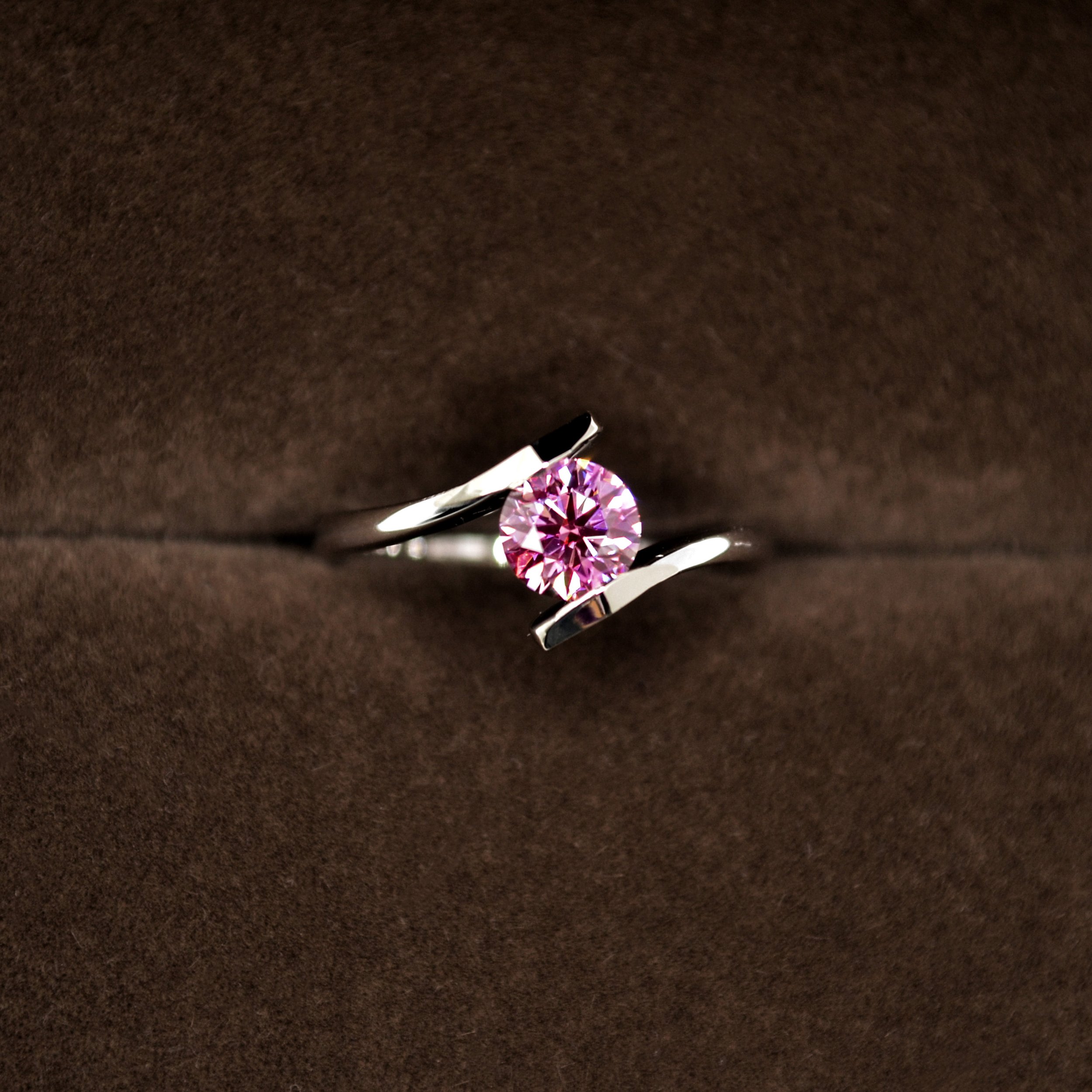 A contemporary platinum cremation ring featuring a stunning round pink diamond, elegantly held by a sleek, open-twist shank design.