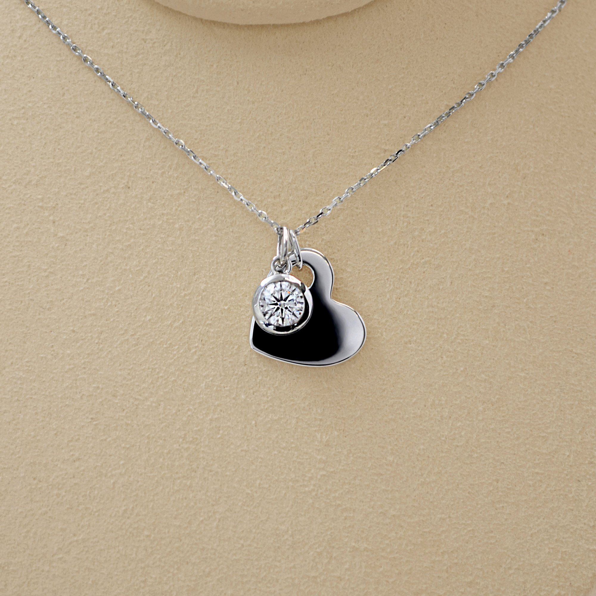 A silver heart-shaped pendant featuring a small round opening, paired with a delicate round diamond, symbolizing how a loved one fills the heart with love and cherished memories.