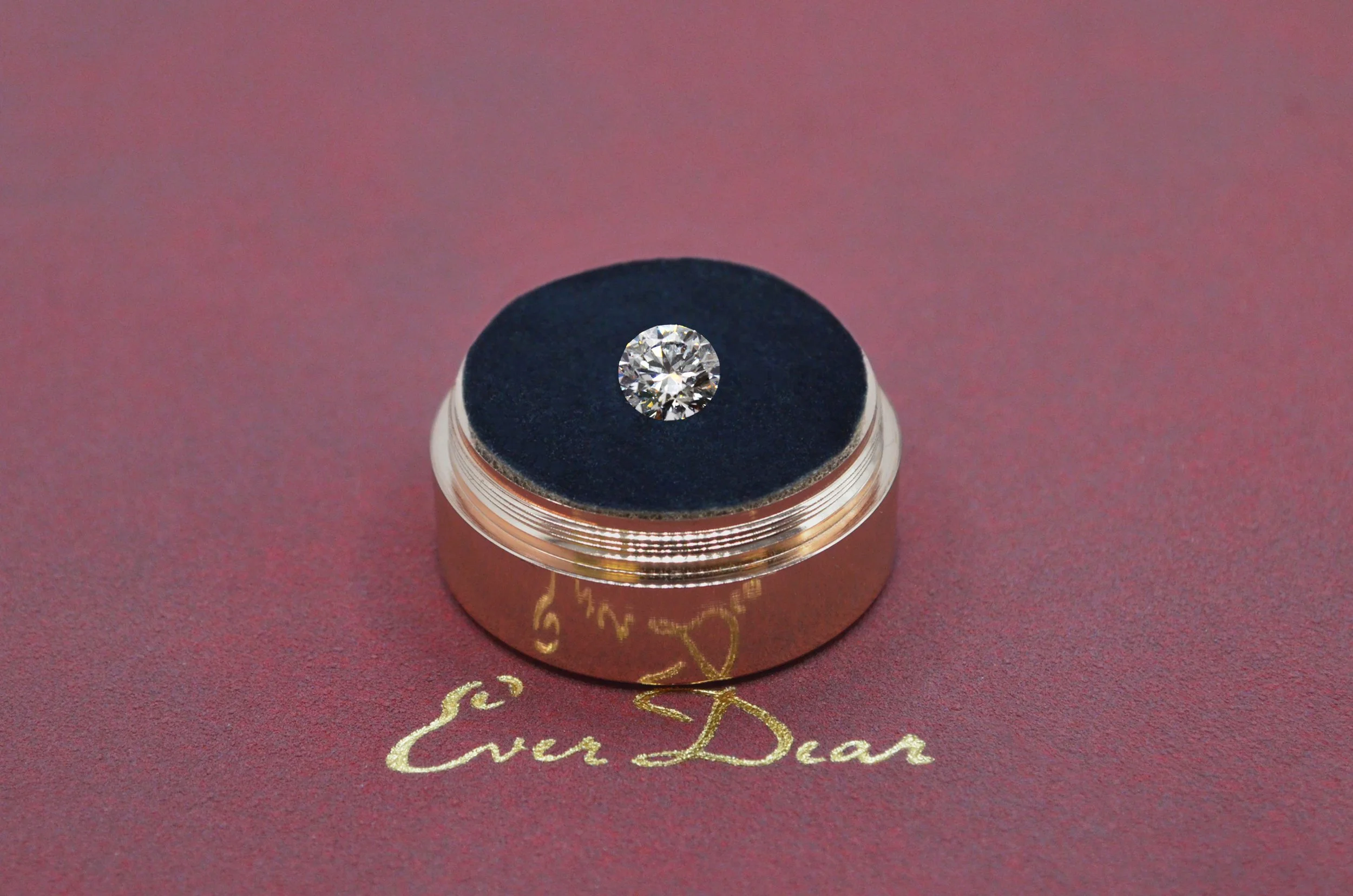 Everdear memorial diamond in a round brilliant cut displayed on a rose gold presentation case with the Everdear logo on a deep burgundy background
