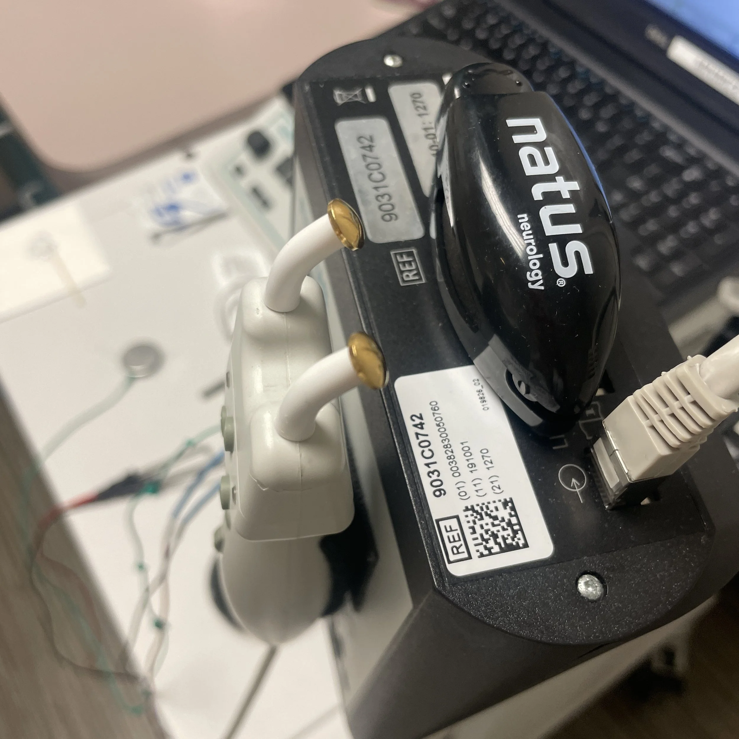 Close-up of a medical device with cables connected, labeled with serial numbers and barcode, and a black component with the label 'technology same.'