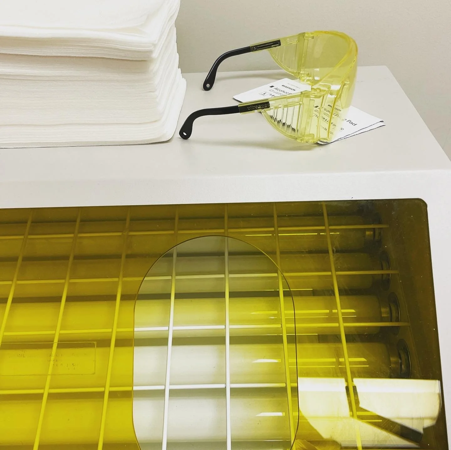 Yellow safety goggles on a white table next to a stack of papers and yellow and black objects inside a yellow cage or container.
