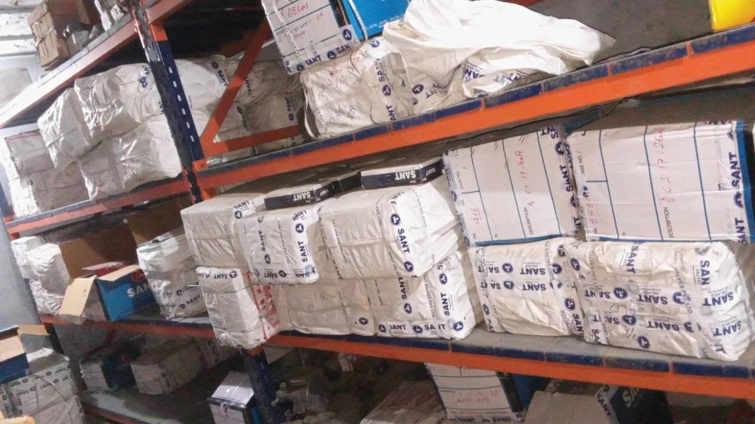 Sant Valves stock on pallet racking at VSC Delhi warehouse — hand-marked dispatch labels with model codes and case numbers
