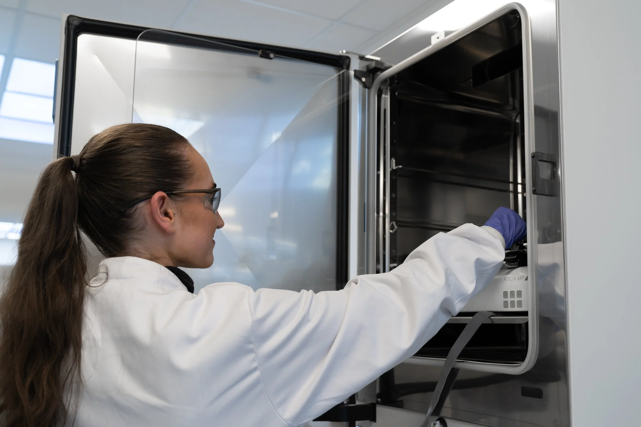 Scientist in lab coat and gloves opening a laboratory incubator in a biotech facility