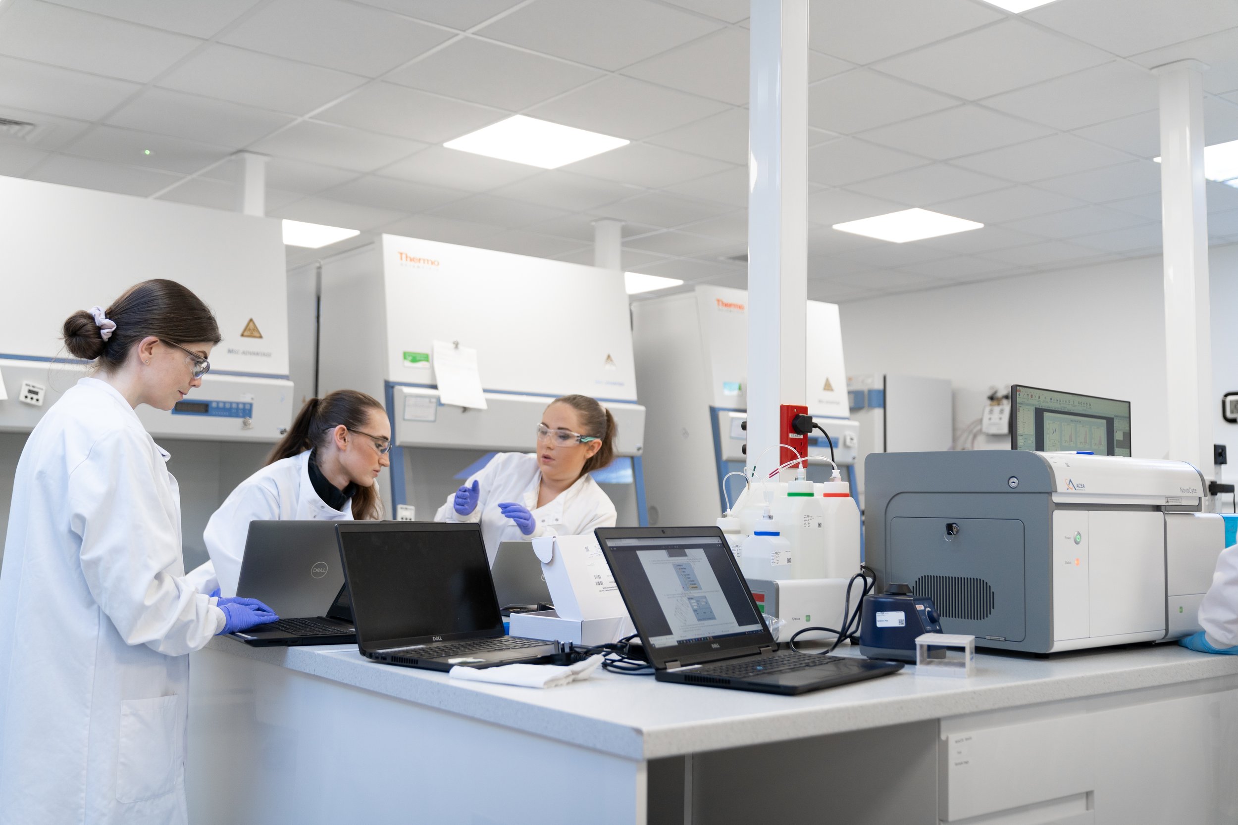 Three scientists reviewing data on laptops together in a biotech lab