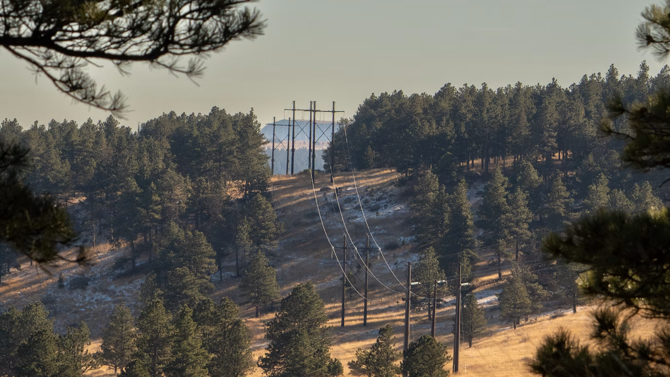 Electric transmission line crossing forested land, with cleared right-of-way corridor visible.