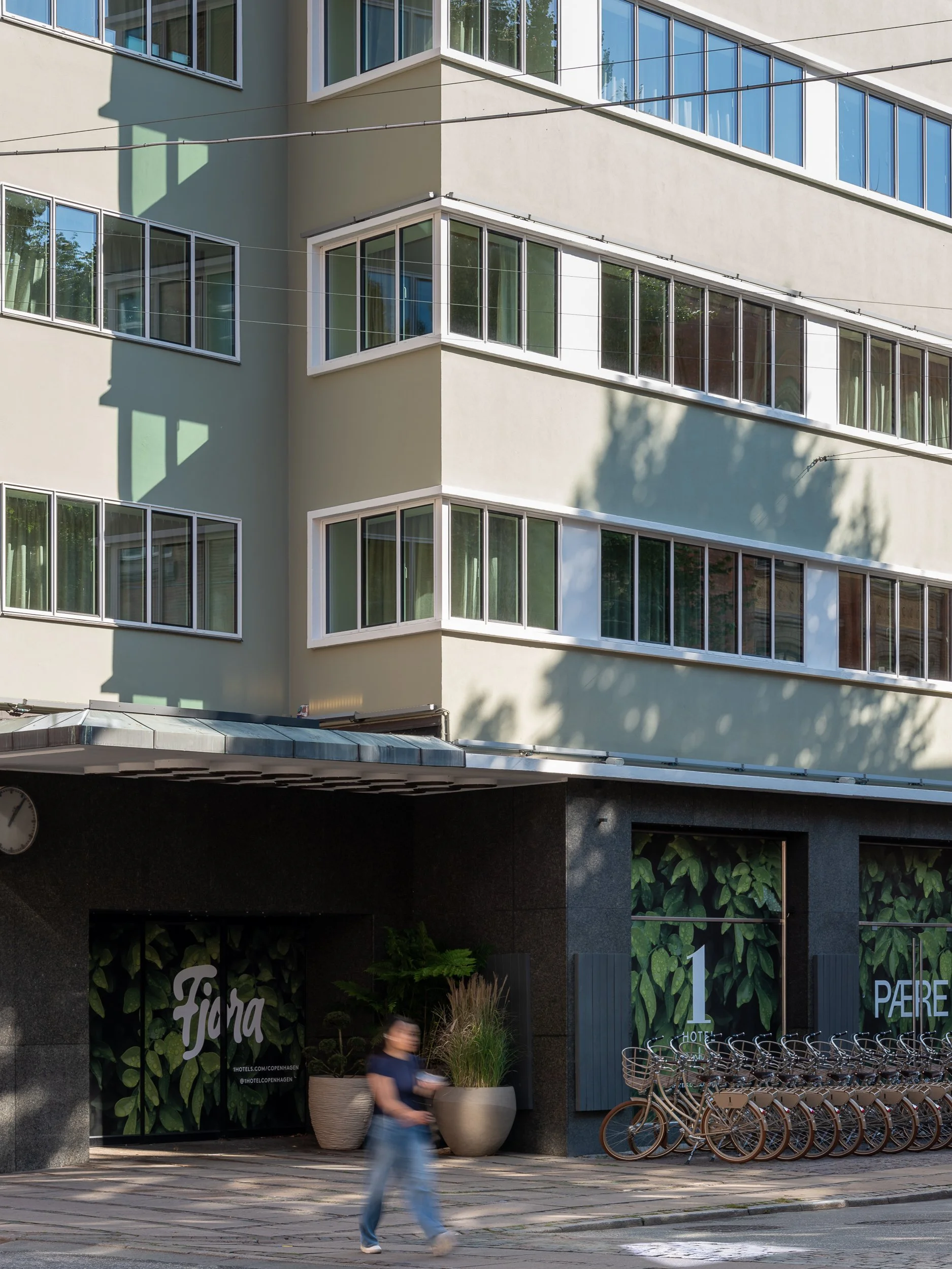 Urban street scene with a modern building featuring large windows, a person walking by, and bicycles parked outside.