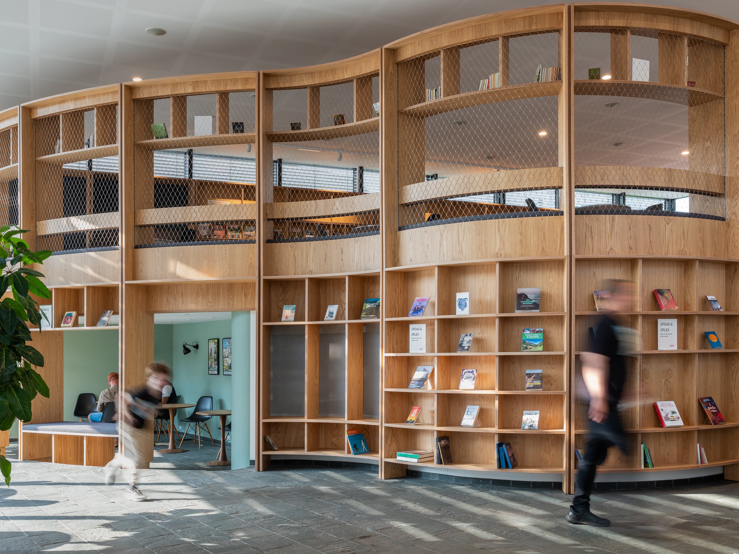 Library interior with curved wooden bookshelves and people walking and sitting.
