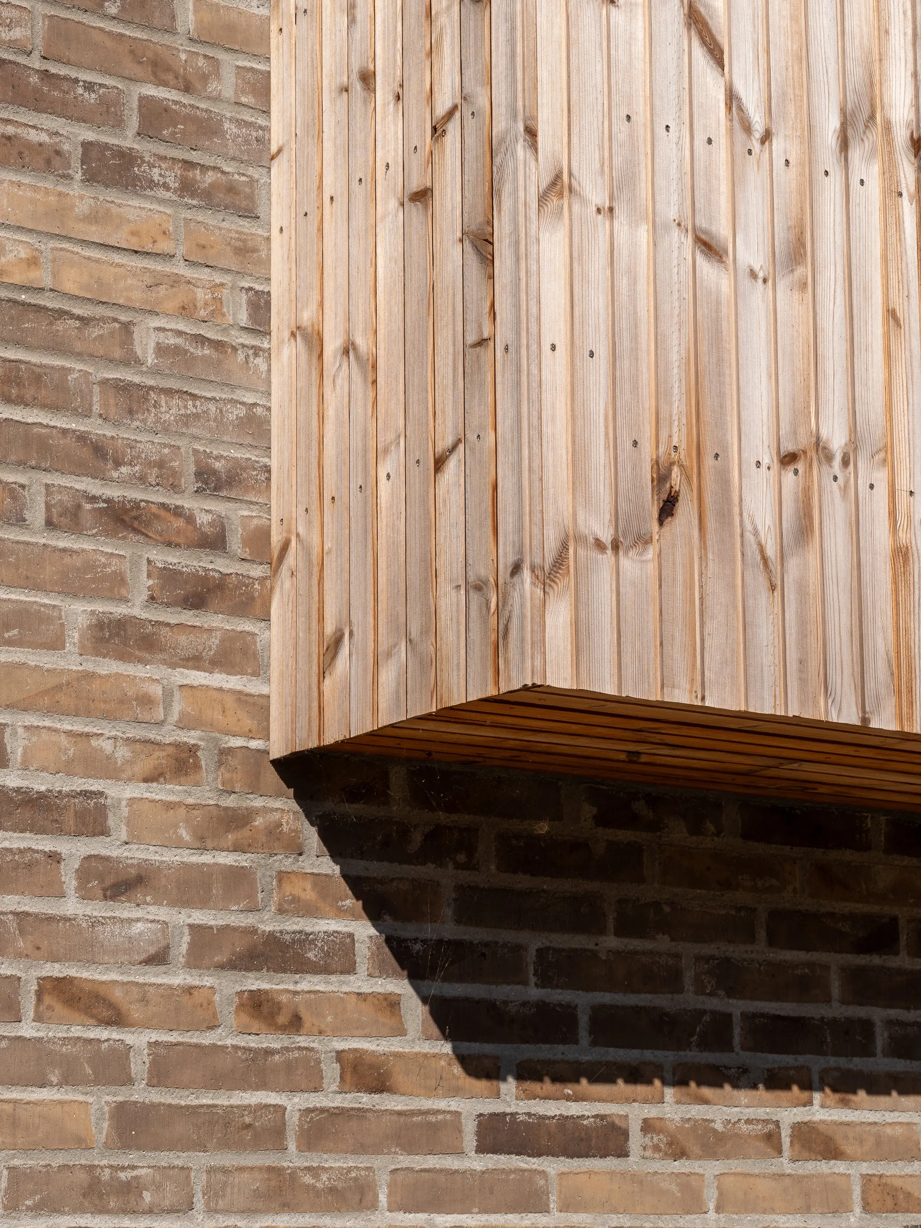 A close-up of a wooden box or cabinet mounted on a brick wall, with the shadow of the box cast on the wall below.
