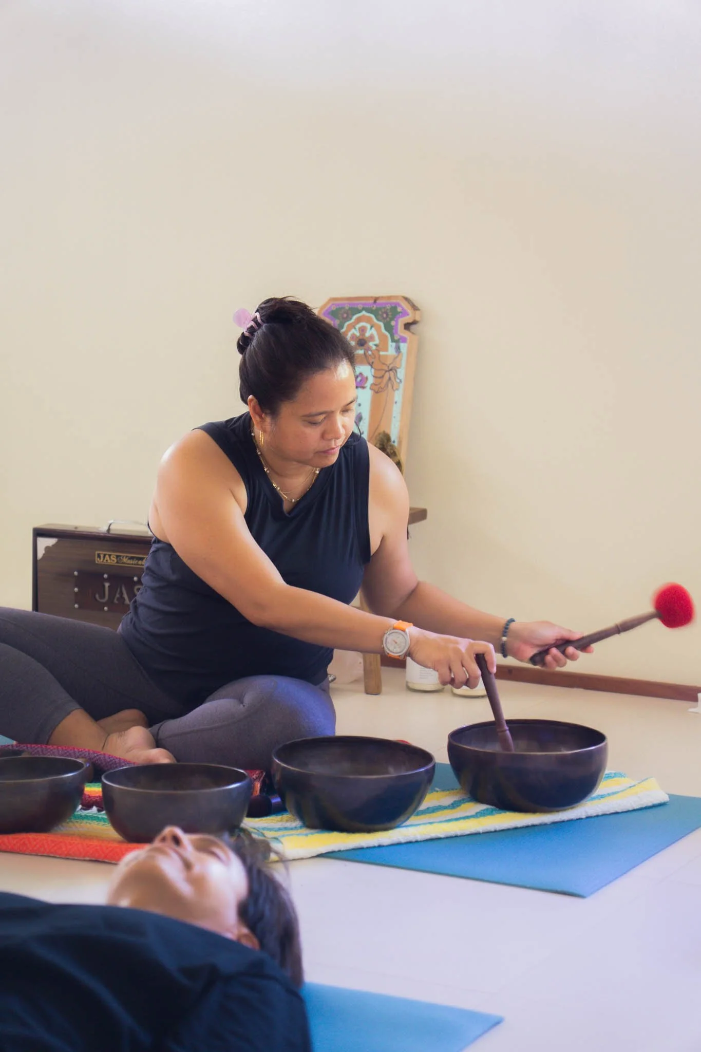 Woman playing singing bowls during a sound therapy session with a person lying on the floor in front of her.