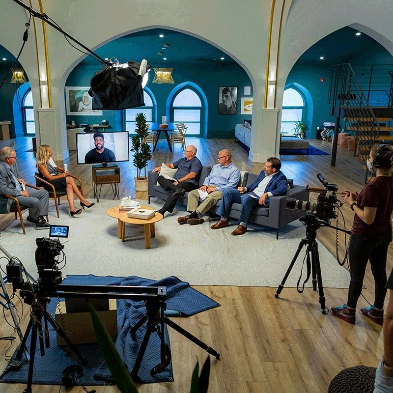 A video production set with 5 individuals sitting on living room furniture.