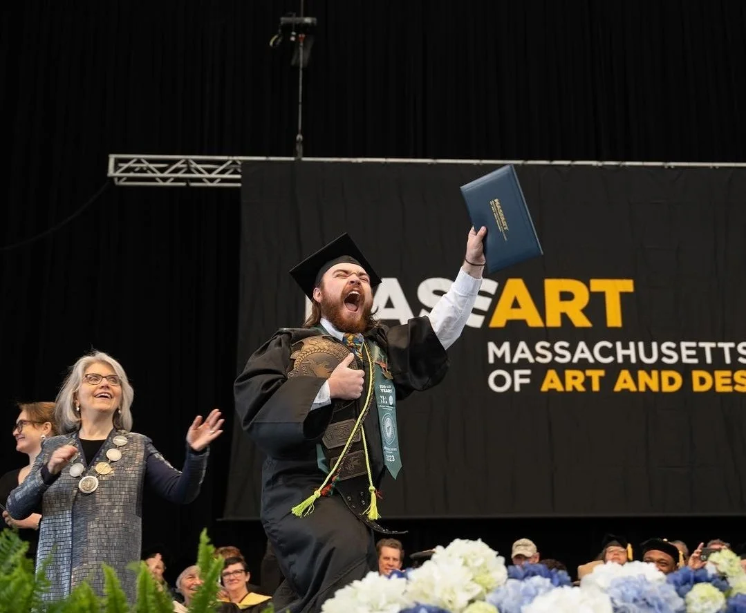 John Intopps celebrating as he receives his diploma from the Massachusetts College of Art and Design. Pictured is also President Mary Grant smiling ath the moment.