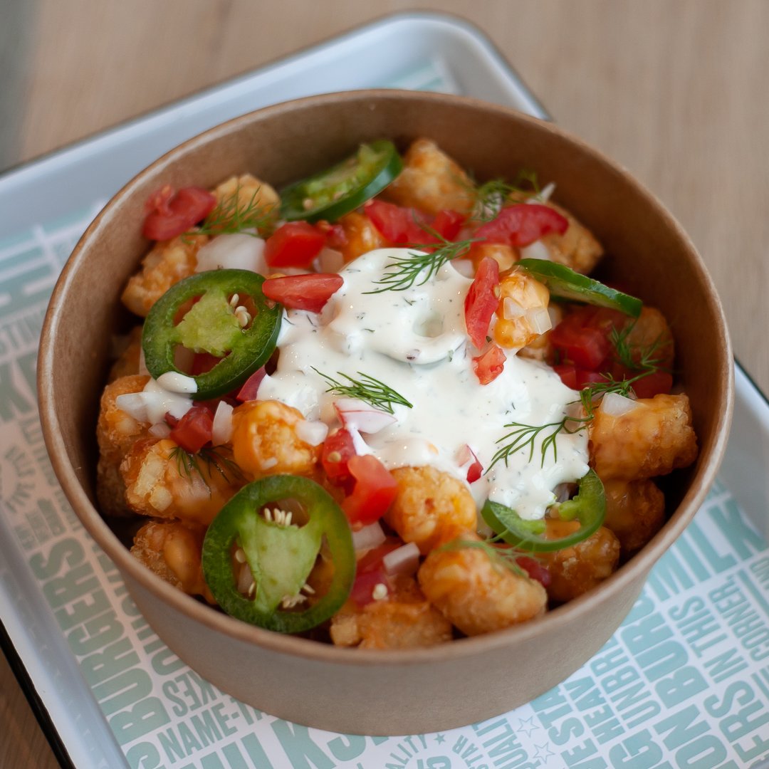 Bowl of loaded tater tots with sour cream, jalapeños, chopped tomatoes, and herbs.