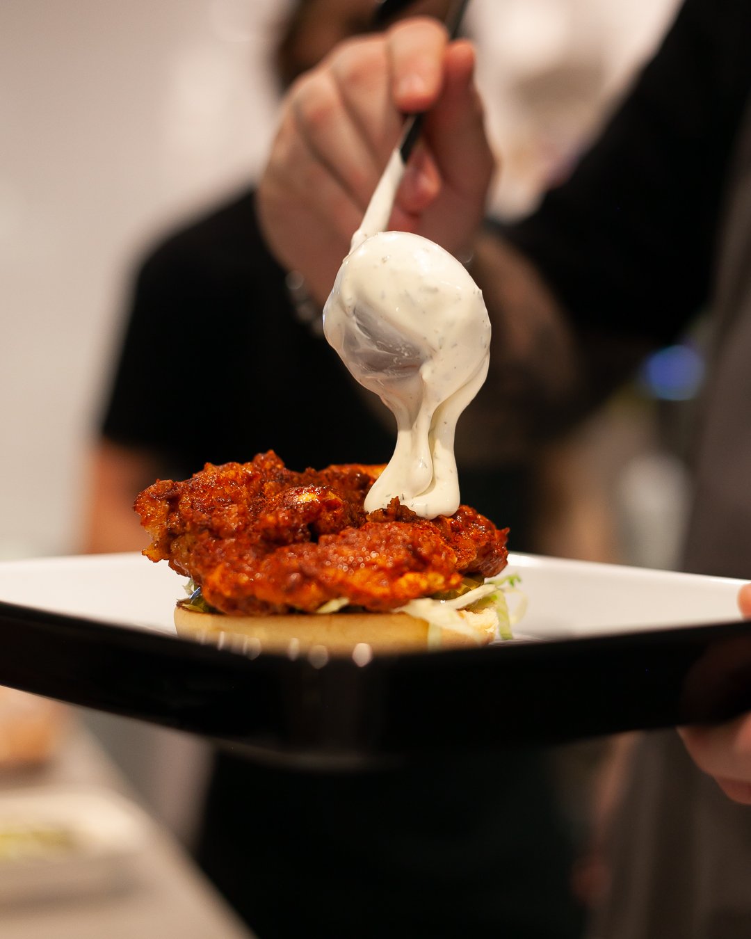 Person holding a plate with fried chicken and a topping of creamy white sauce being poured over it.