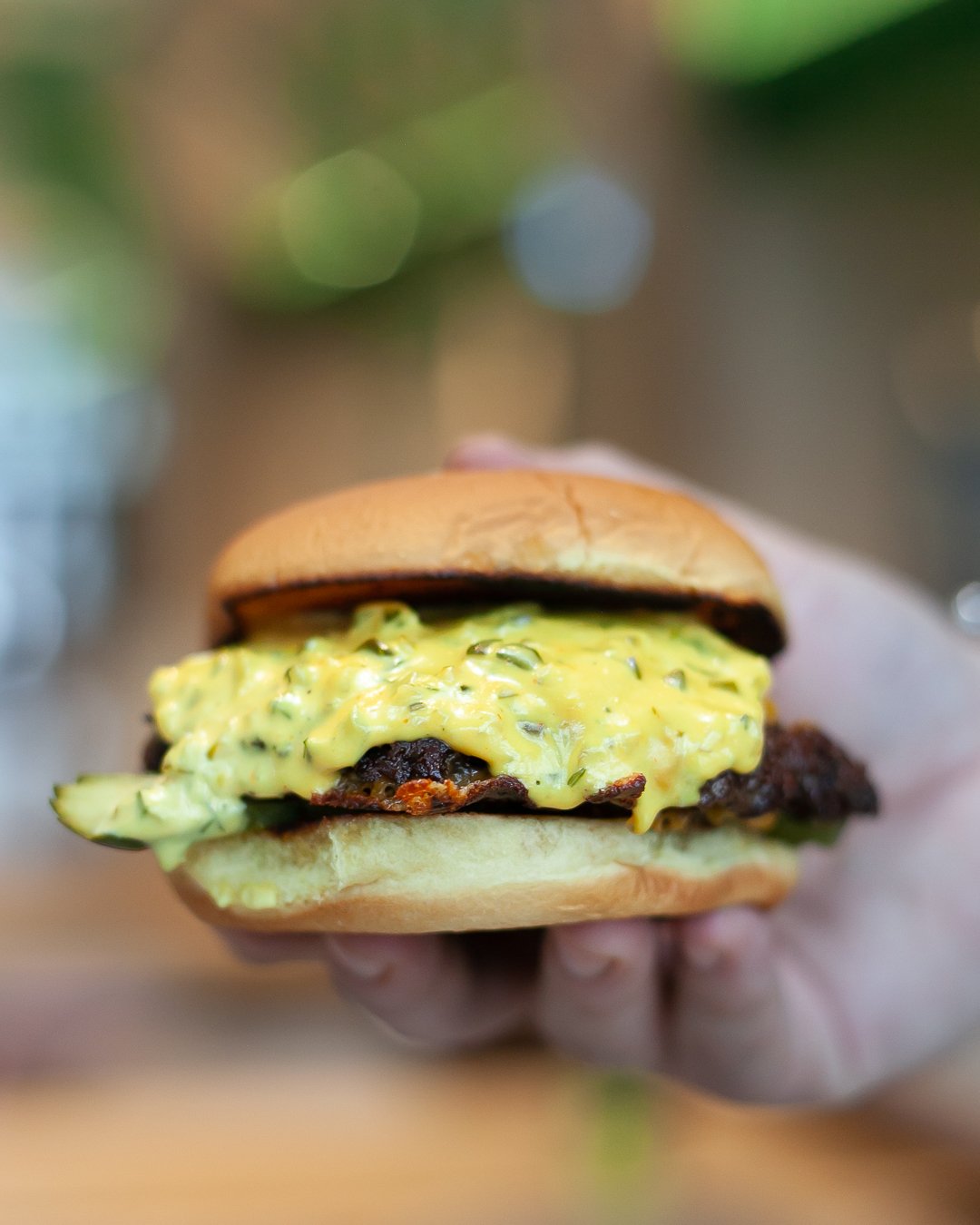 Close-up of a sandwich with scrambled eggs and melted cheese, held in a hand. The background is blurred with lights.