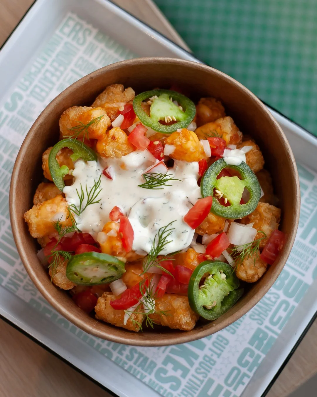 Bowl of fried chicken bites topped with pico de gallo, sliced jalapeños, fresh dill, and creamy sauce, served on a tray.
