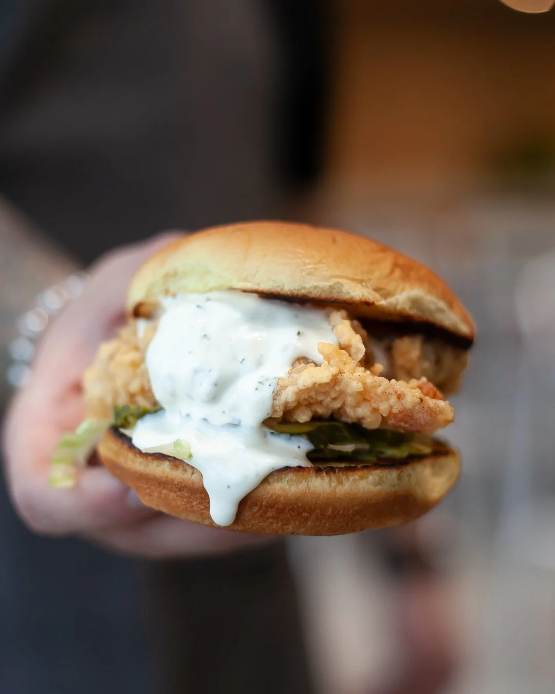 Close-up of a sandwich with fried chicken, lettuce, and white sauce in a bun.