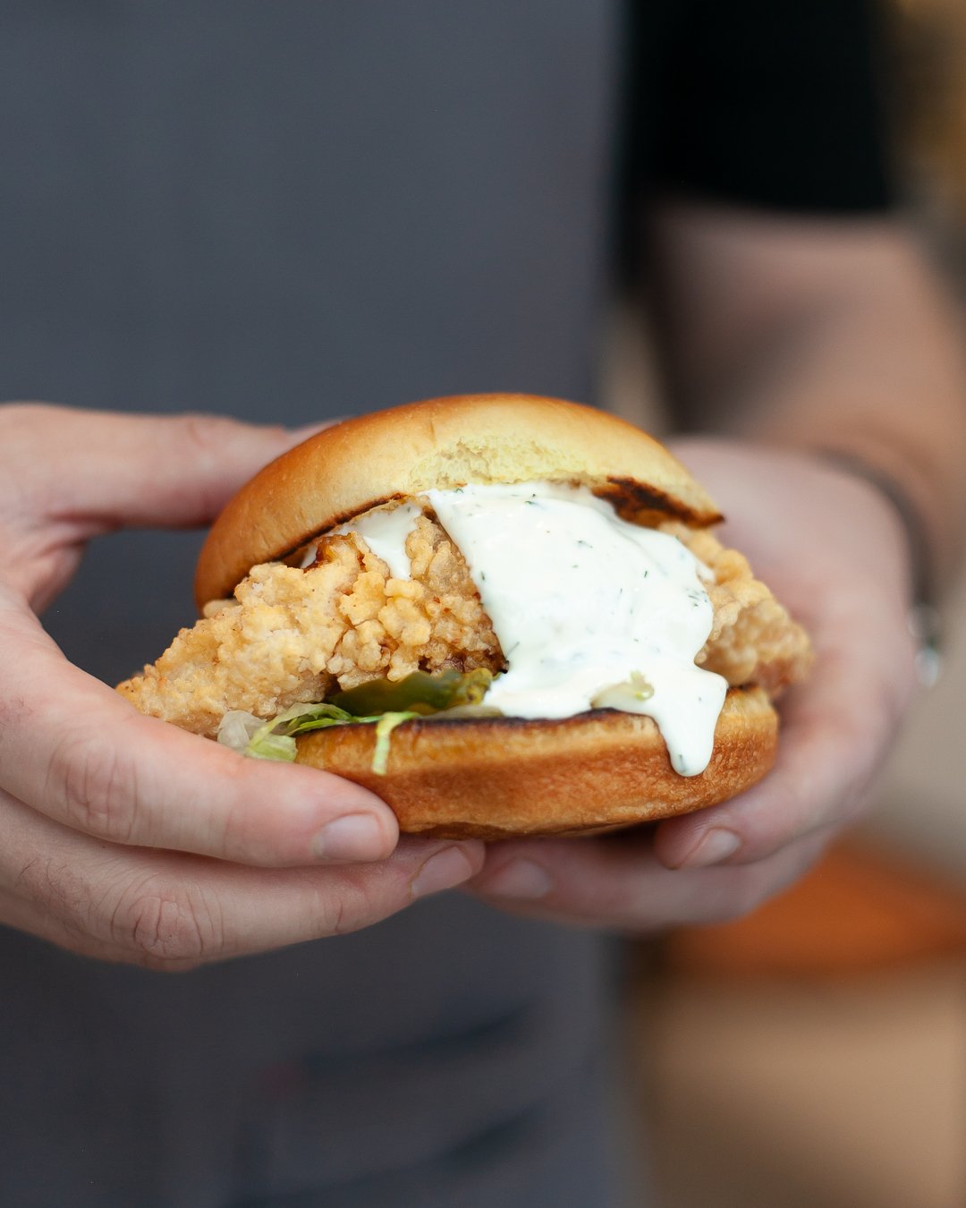 Person holding a fried chicken sandwich with lettuce, mayonnaise, and a soft bun.