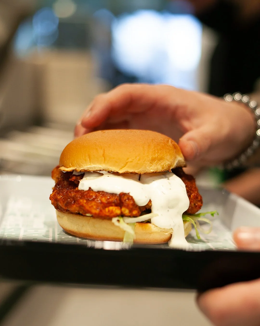 Close-up of a hand holding a fried chicken sandwich with lettuce, mayonnaise, and a soft bun.