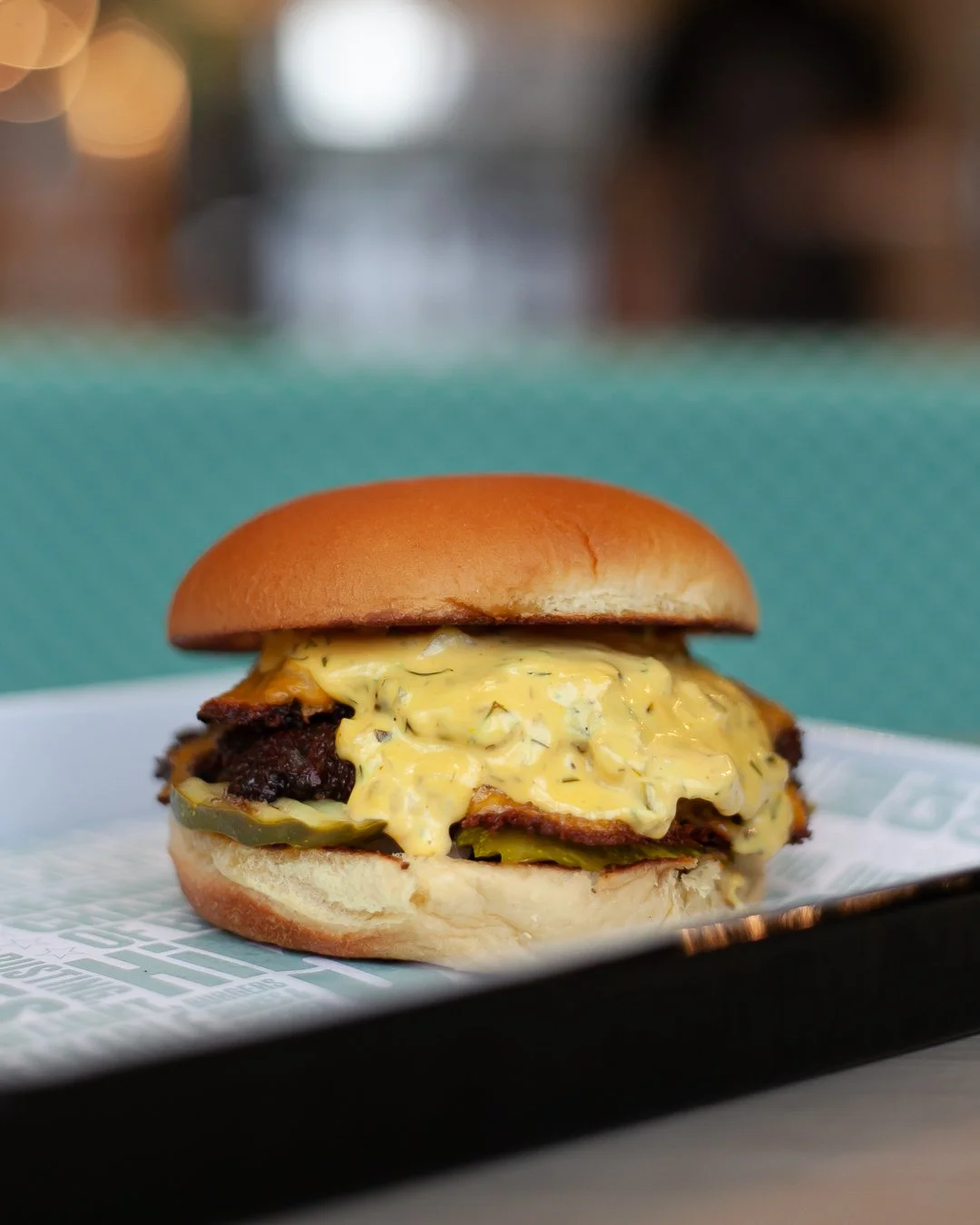 A cheeseburger with pickles and a spicy sauce, served on a bun.