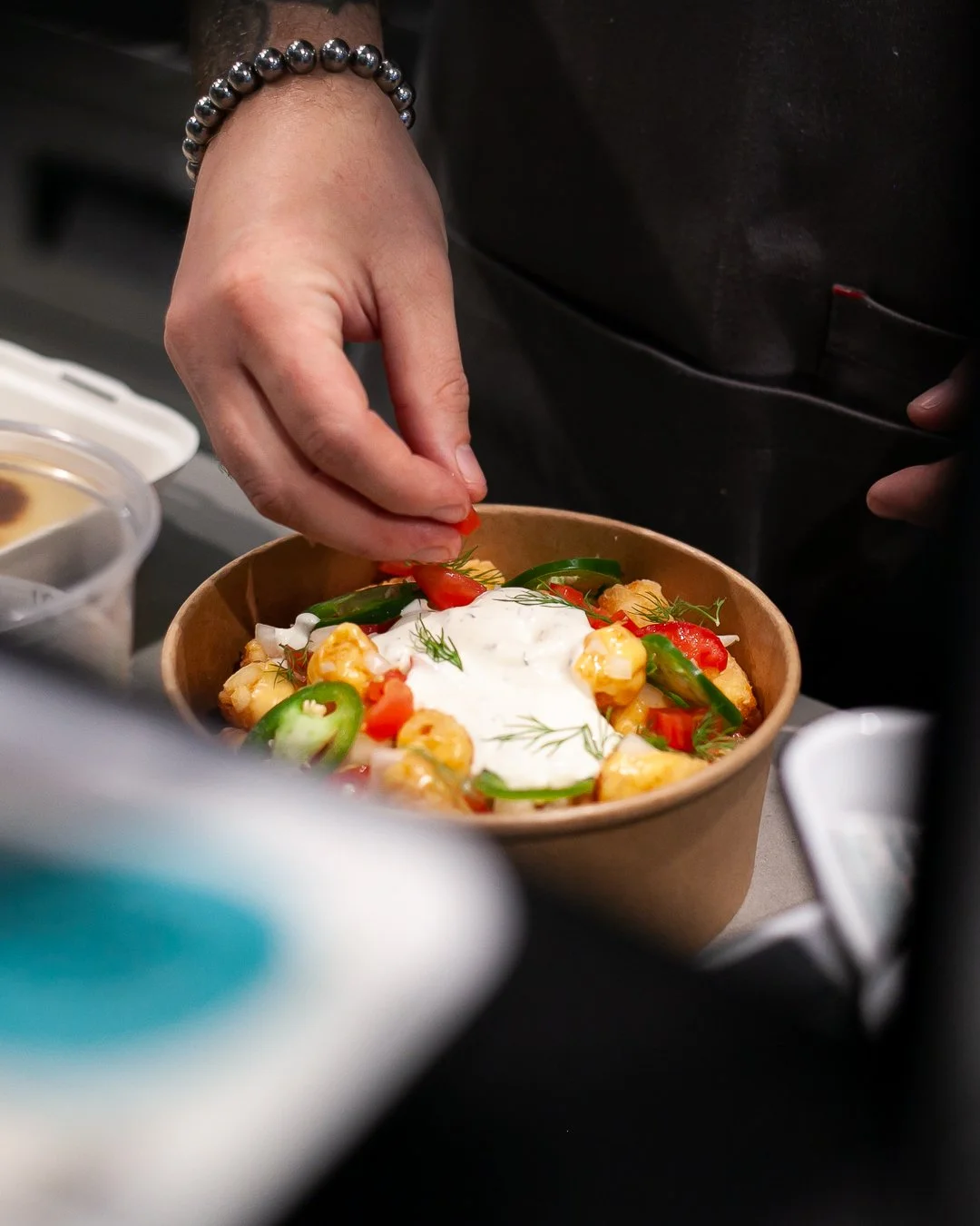 A hand garnishing a bowl of food with fresh herbs, surrounded by ingredients on a countertop.