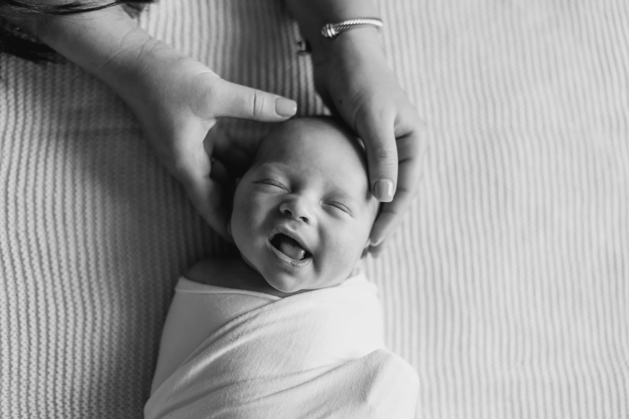 A black and white photo of a baby lying on a textured surface, with a person gently holding the baby's head. In-home Newborn session photographed by Vanessa Underwood, newborn photographer serving Amarillo and surrounding areas.
