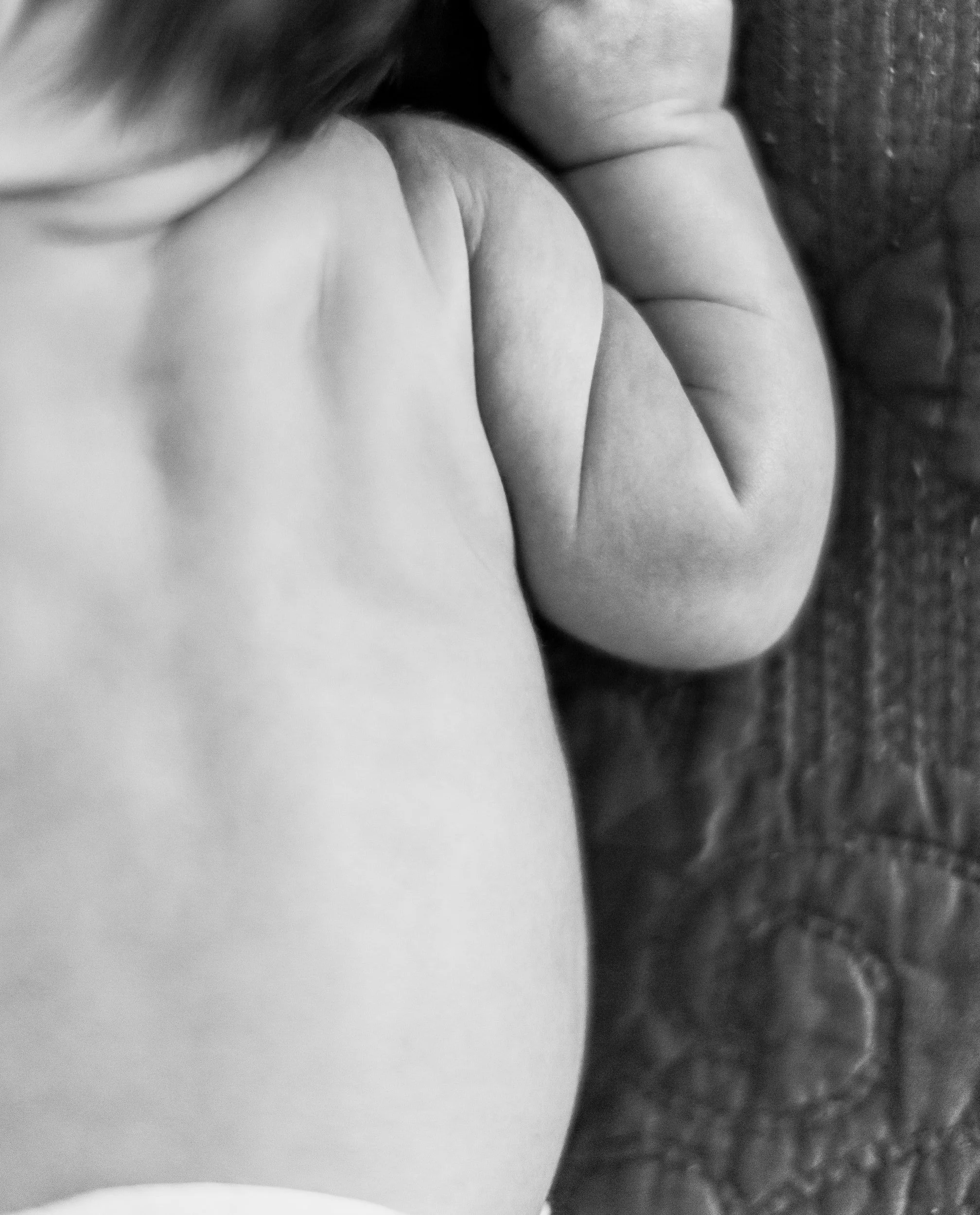 Close-up black and white photo of a baby lying on a textured surface, showing the baby's face, hand, and part of their body. In-home Newborn session photographed by Vanessa Underwood, newborn photographer serving Amarillo and surrounding areas.