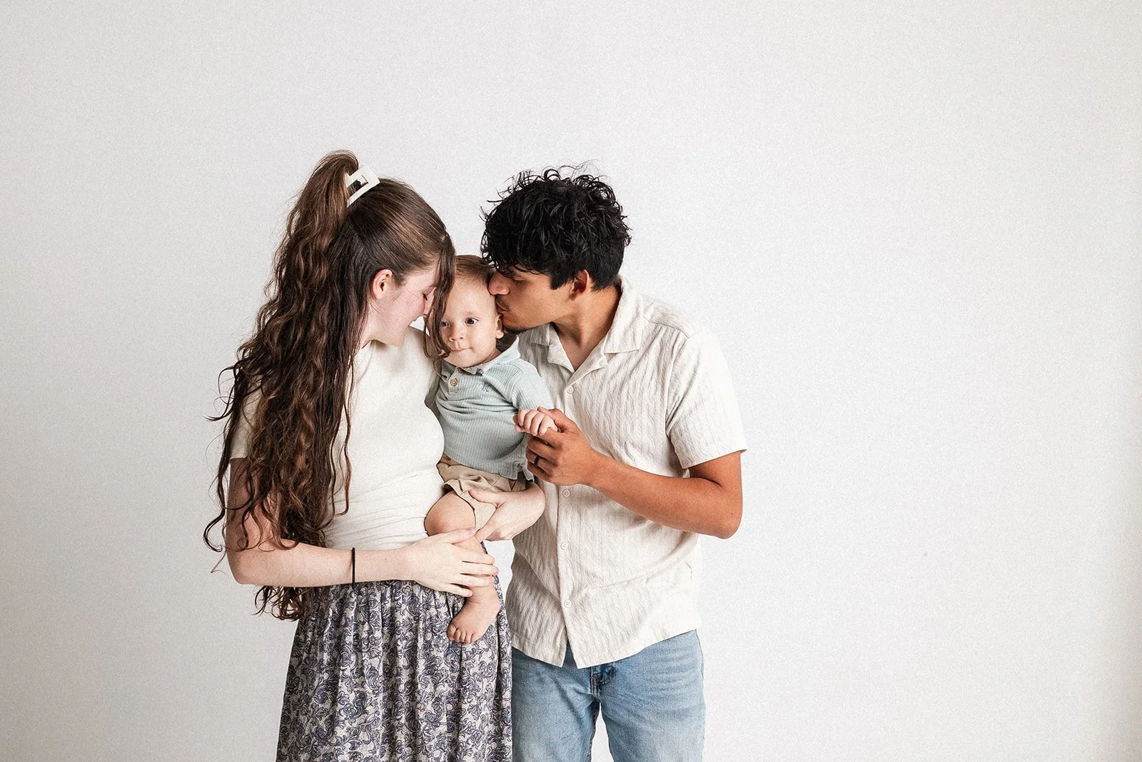 Family of three holding and kissing their baby against a plain white background. Portrait at Vanessa Underwood Photography, a studio near downtown Amarillo, Texas.