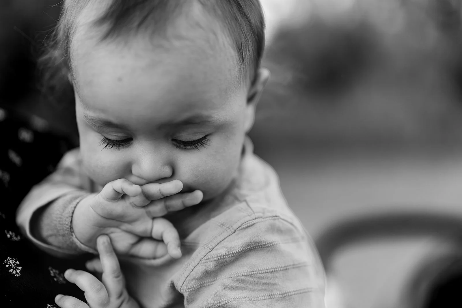 A young child with closed eyes, holding her hand near her mouth, in black and white.