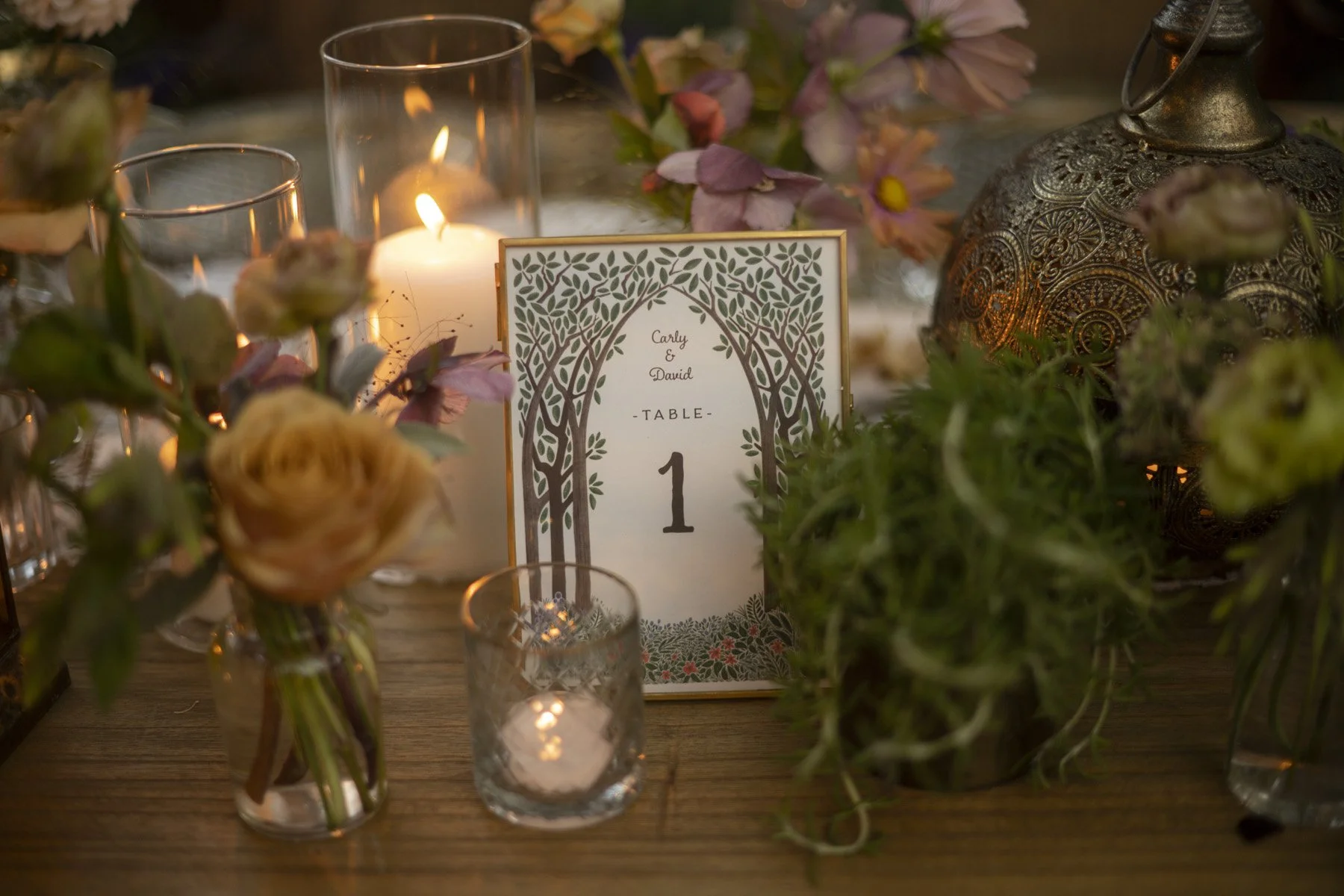 A table number sign inspired by the elves of lord of the rings placed among pink florals, potted plants, and glowing candles in The Oak Room at Calamigos Ranch Malibu