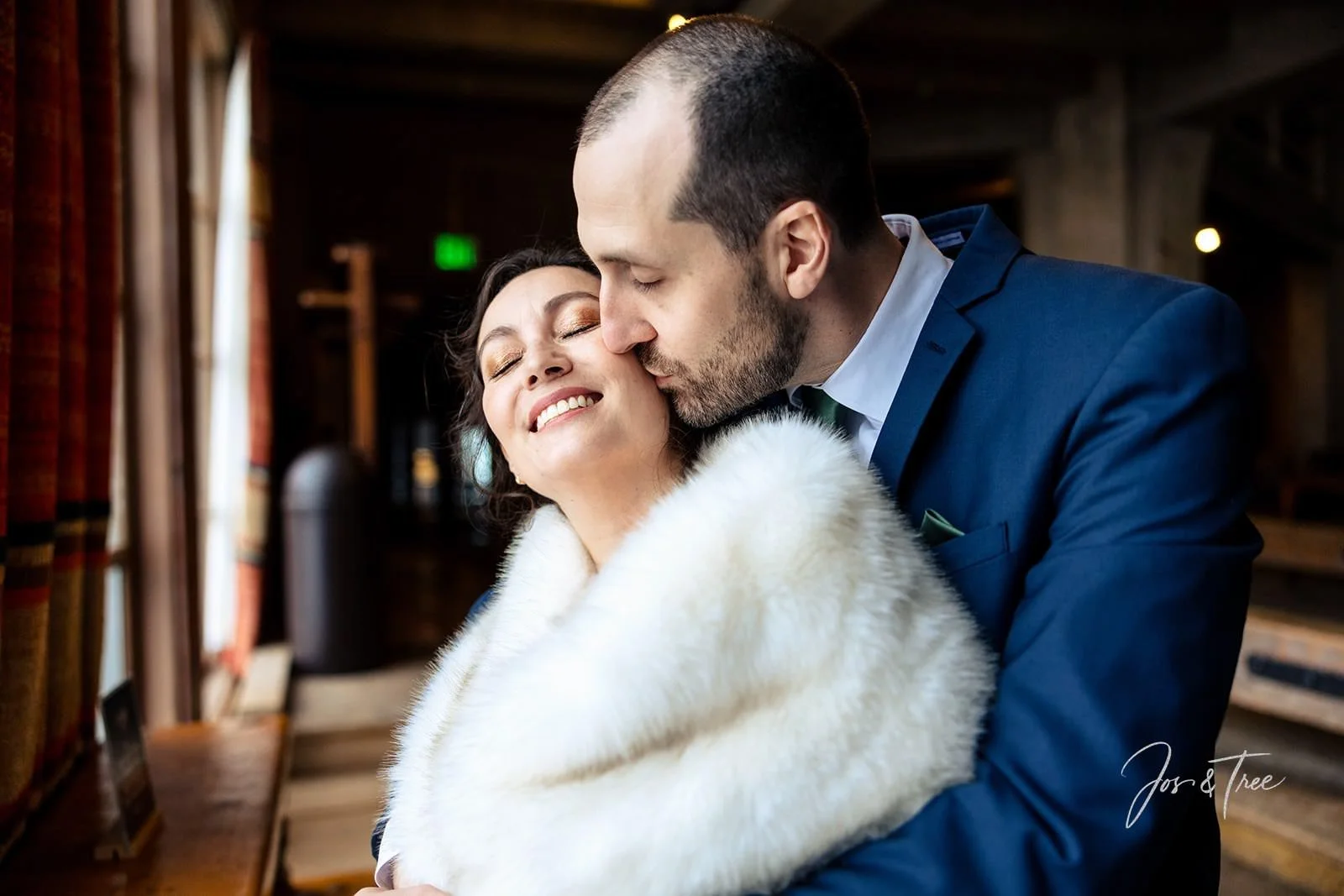 bride-wrapped-in-a-fur-being-kissed-on-the-cheek-by-groom.jpg