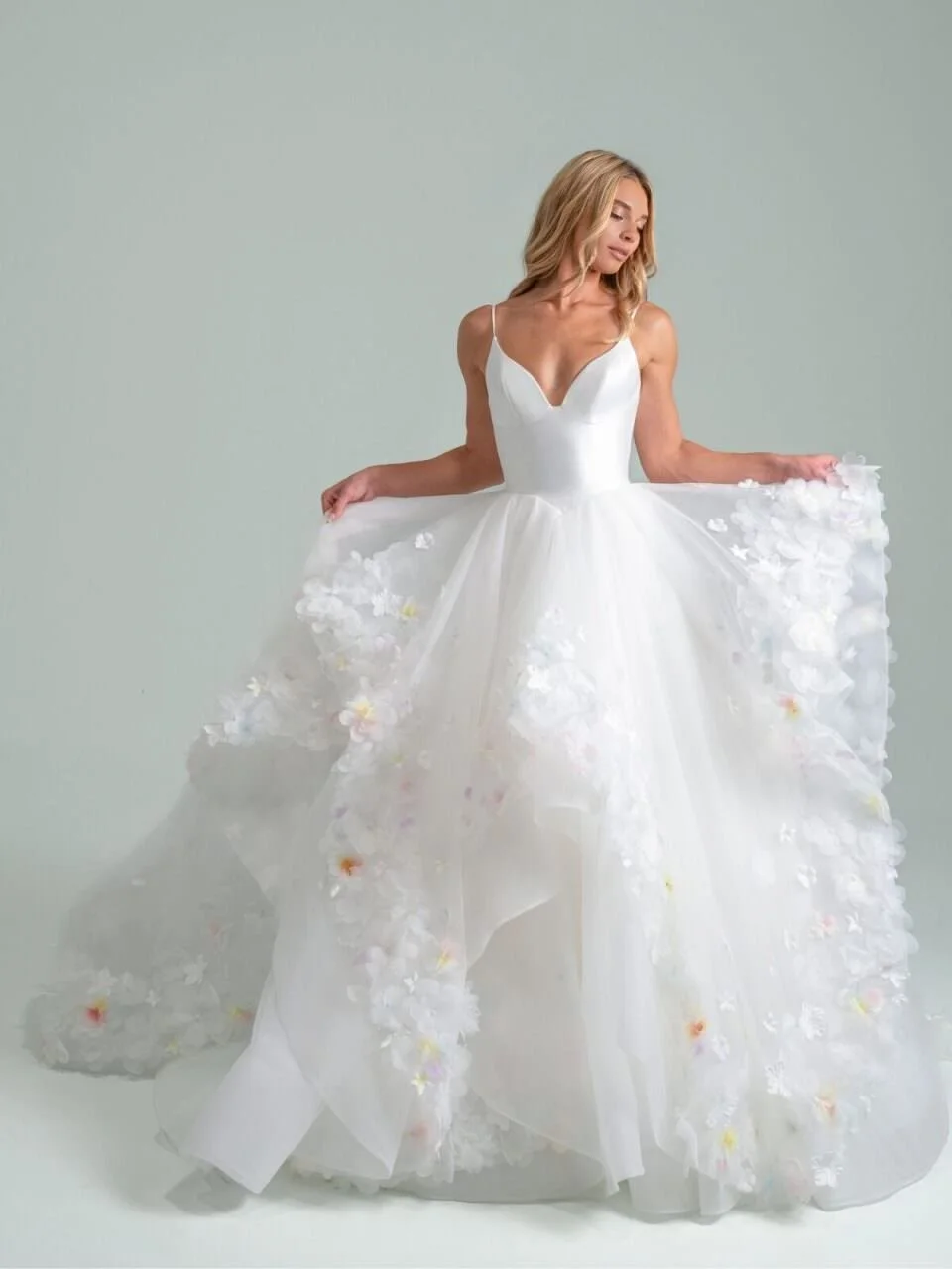 blonde model wearing a layered ballgown with pastel 3D floral appliques in front of white backdrop