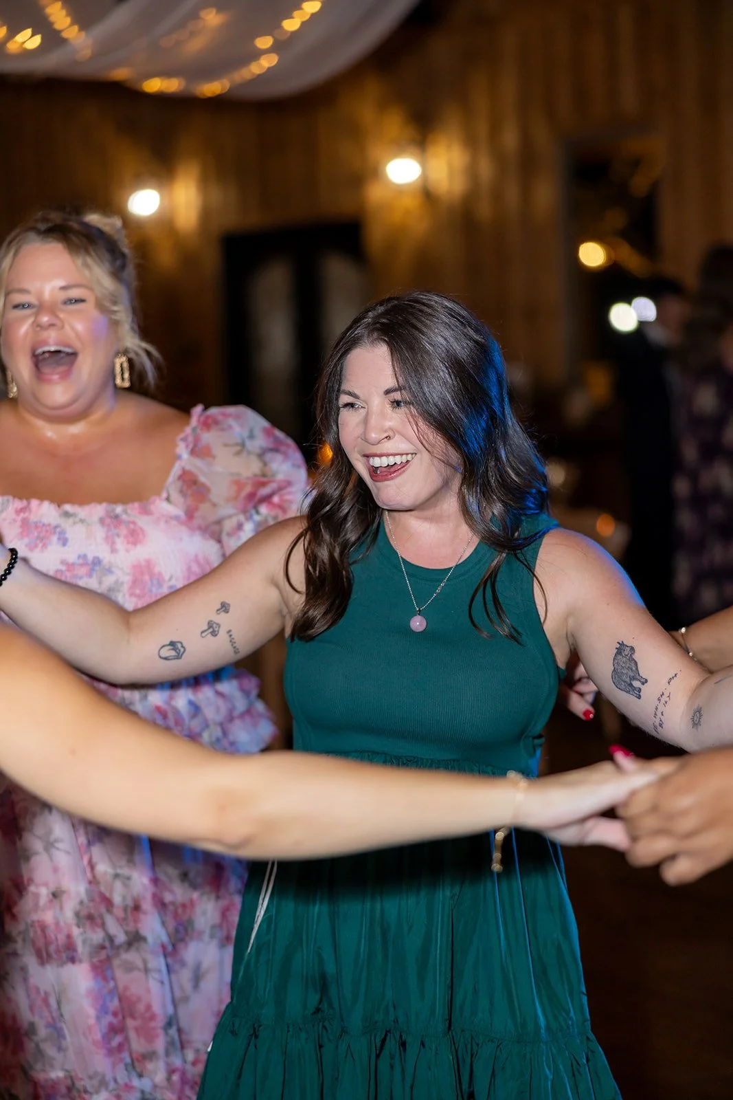Two women dancing and smiling at a celebration in a wooden decorated venue.