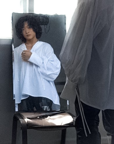 A woman with curly hair wearing a white shirt looking into a mirror.