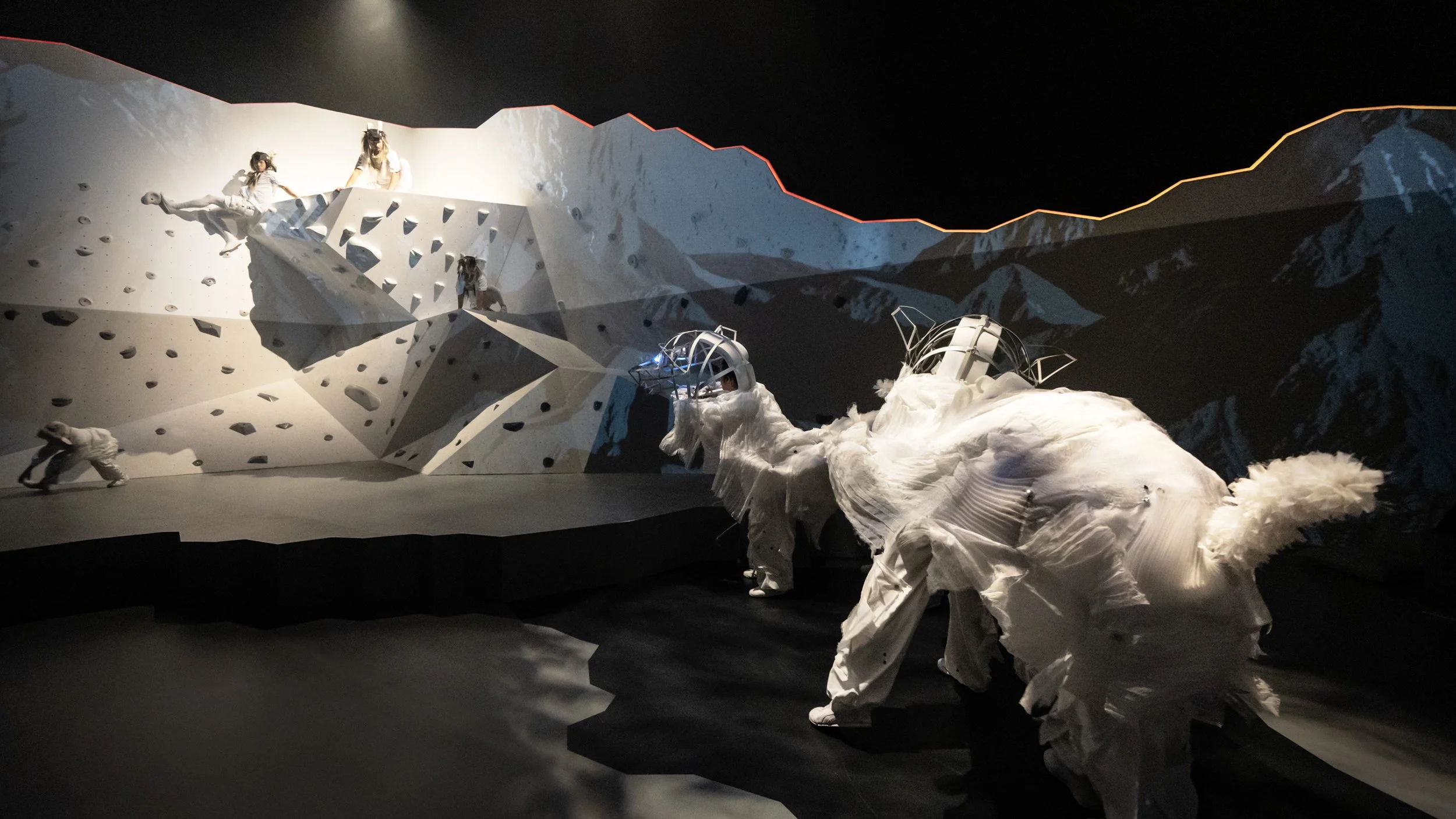 Performers in vivid projection landscape on geometric mountain set, immersive design by Ruby Law RULA