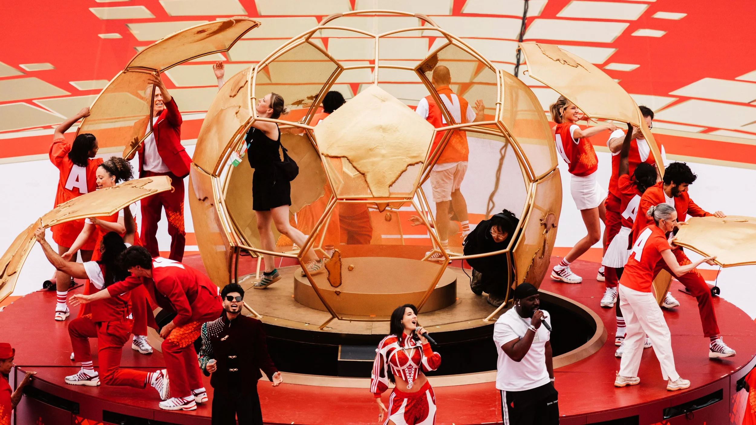 The Golden Sphere opens during rehearsal as performers assemble around the structure, revealing the internal performance platform and transforming scenic