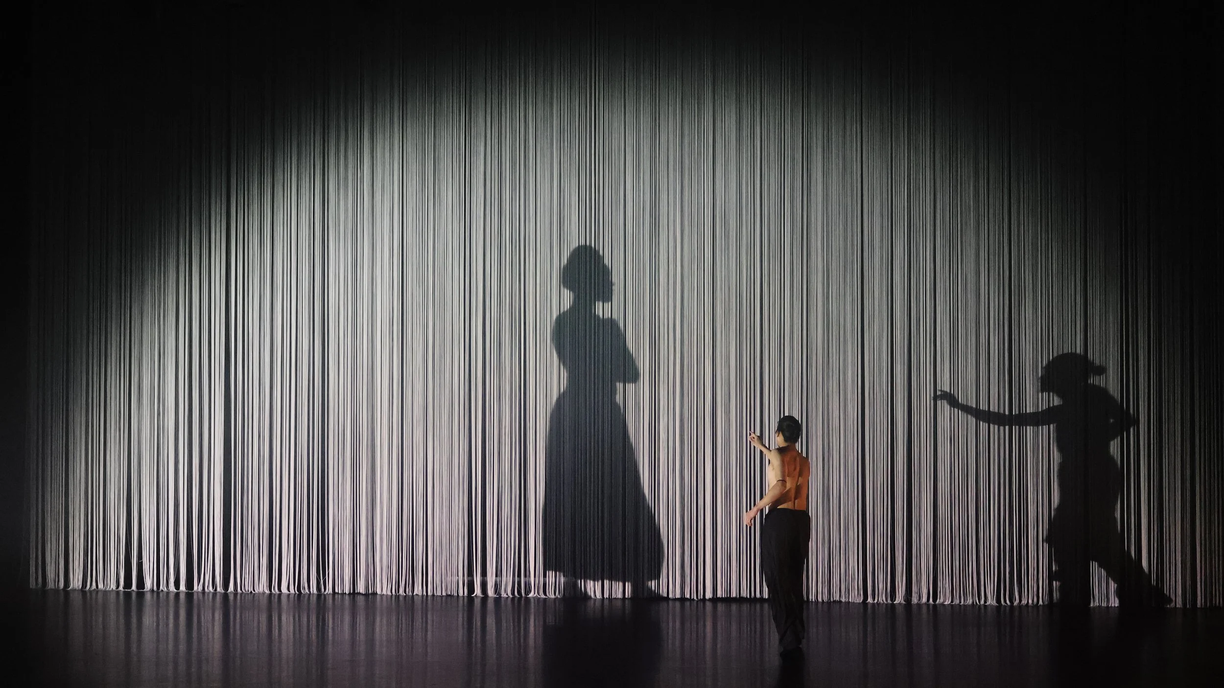 Dancer casting large shadow across vertical string curtain in Tellus by Dickson Mbi, contemporary dance stage design by London set designer Ruby Law.