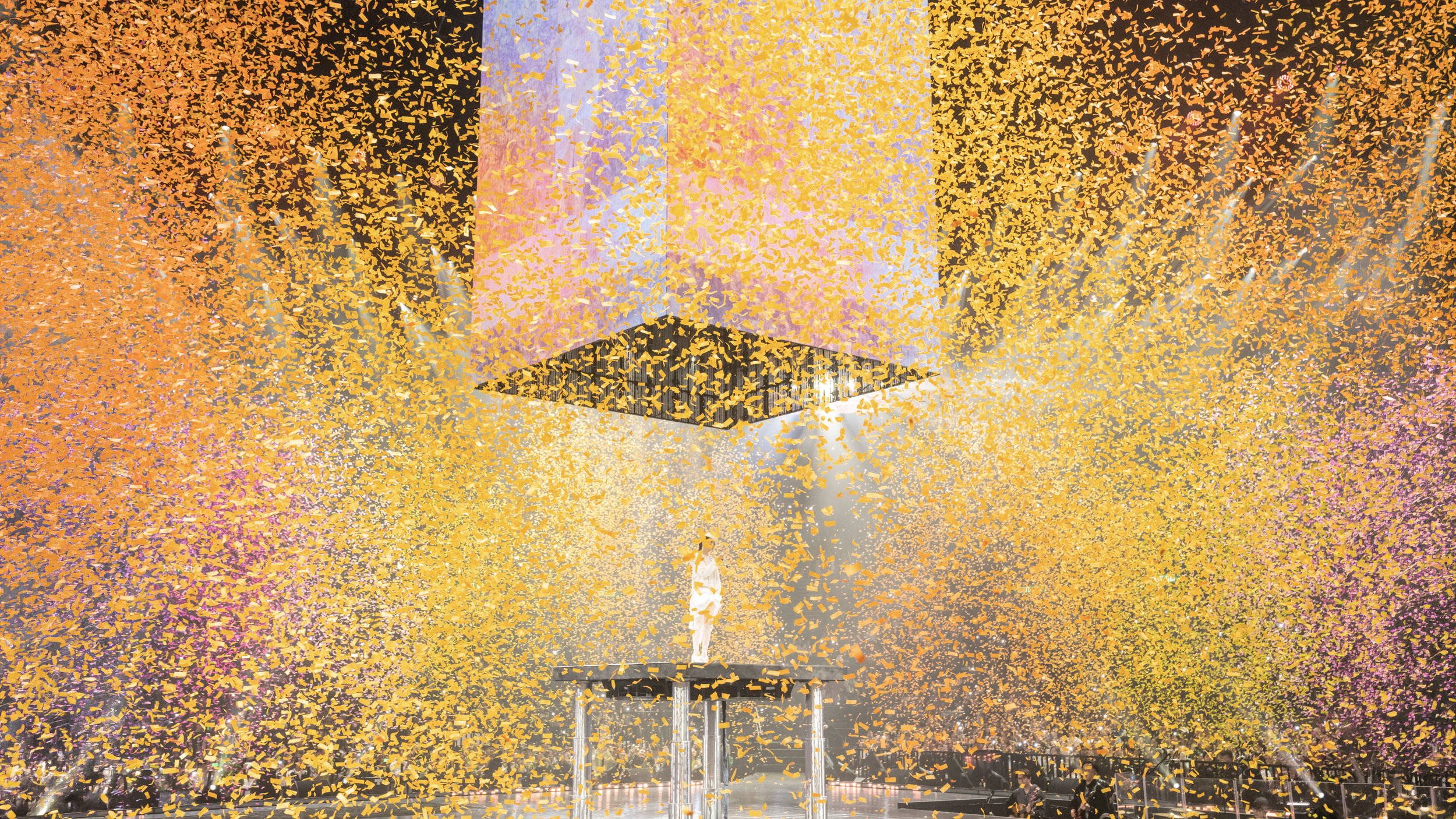 Jace Chan on elevated platform under suspended LED cube as golden confetti fills arena in Jace World concert, immersive pop stage design by London set designer Ruby Law.