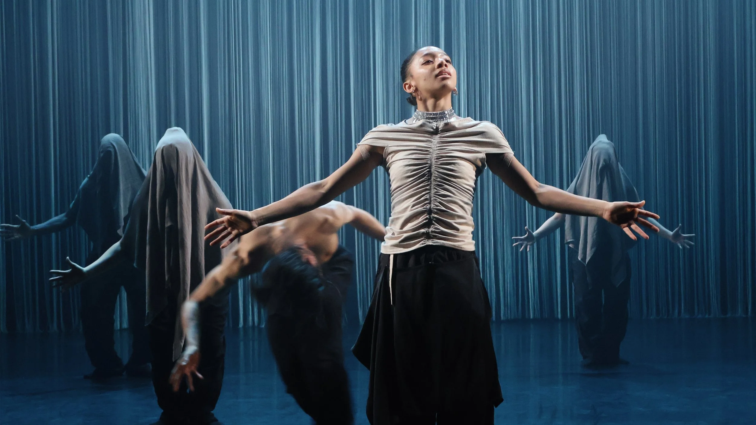 Dancer reaching outward before textured vertical string curtain in Tellus by Dickson Mbi, contemporary dance stage design by London set designer Ruby Law.