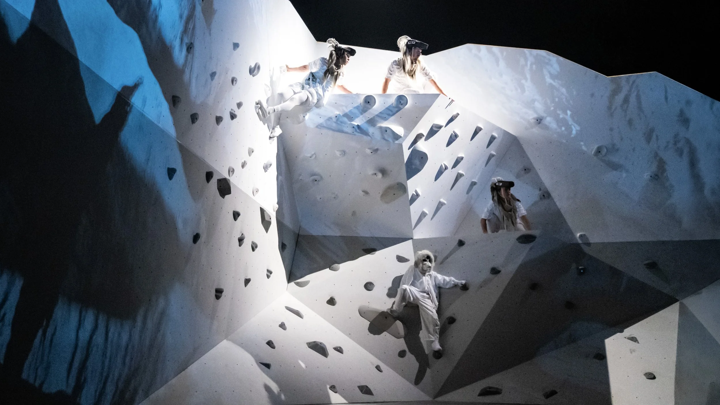 Performers climbing angular snow landscape set, innovative immersive design by Ruby Law RULA London set designer