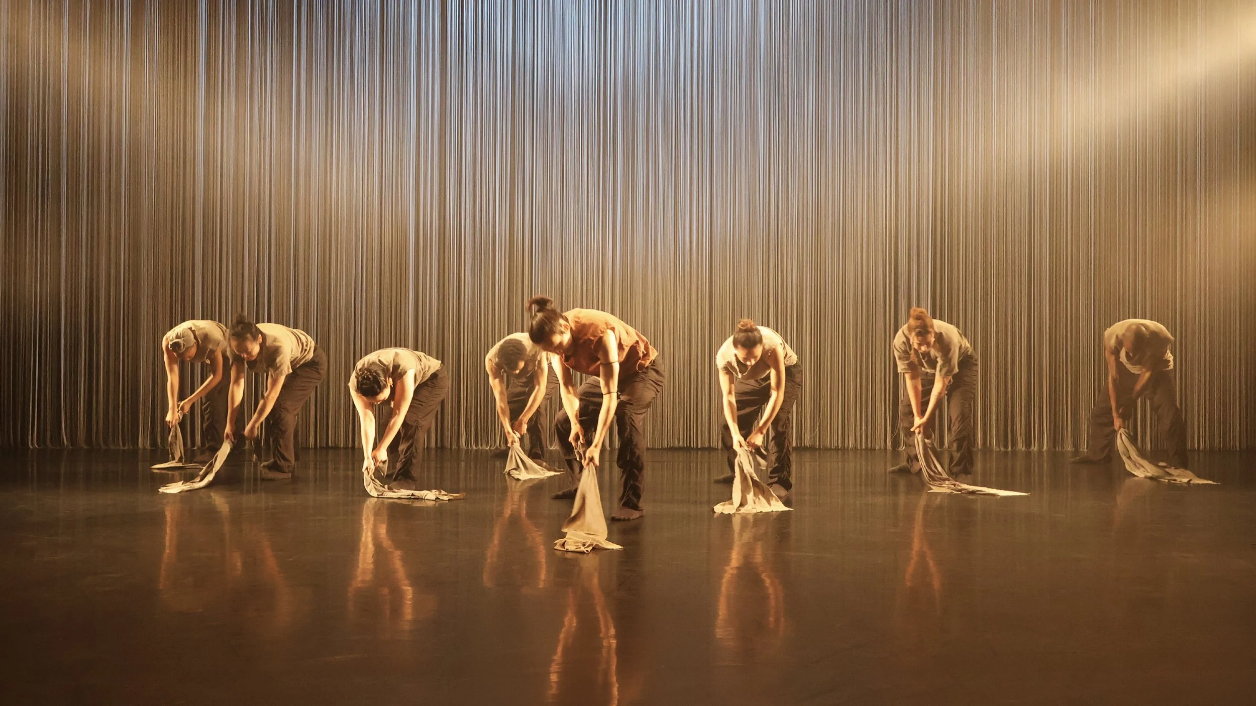 Ensemble performing in warm amber light against vertical string curtain backdrop in Tellus by Dickson Mbi, stage design by London dance set designer Ruby Law.